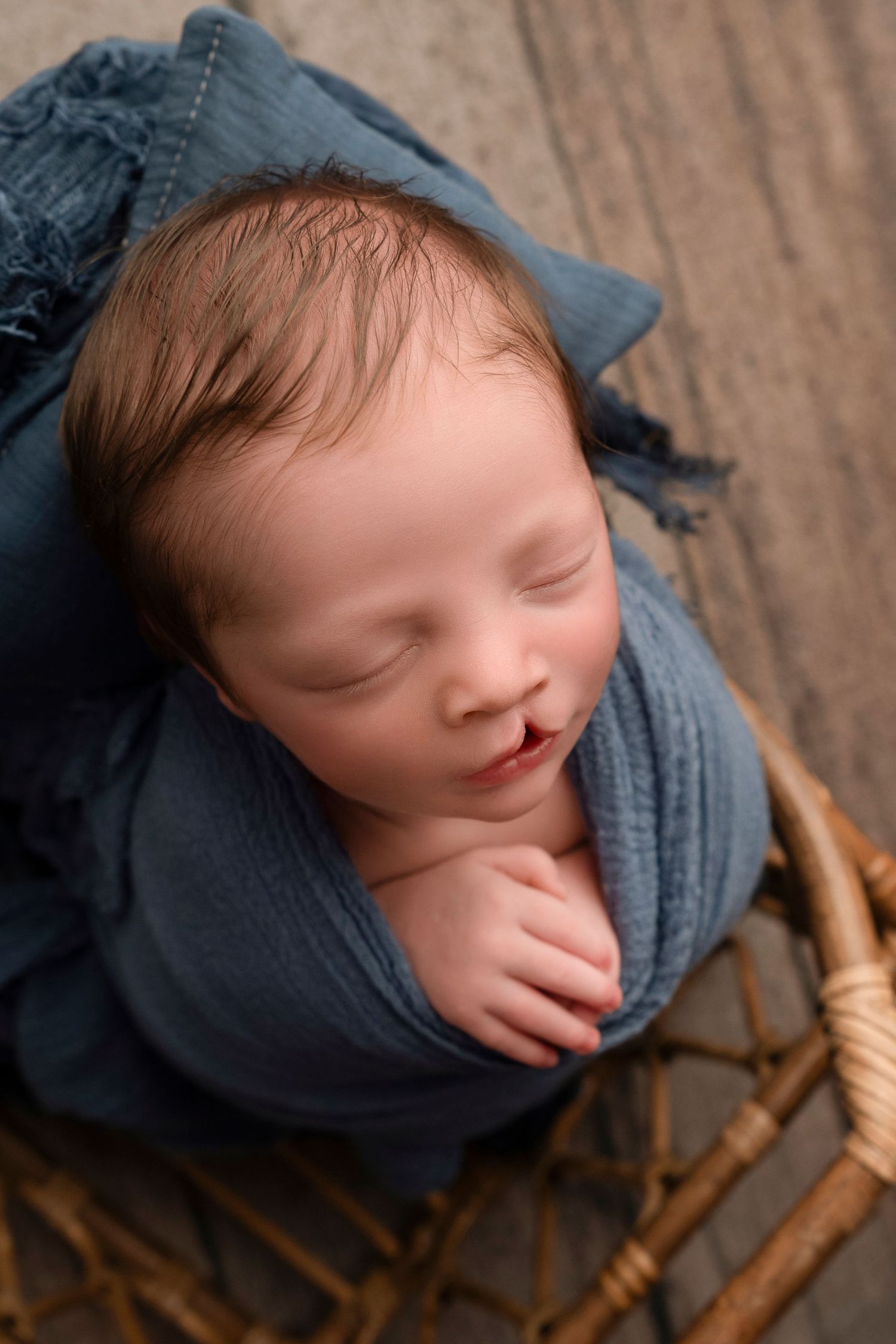 A sleeping baby in a gray sweater rests peacefully on a wooden rocking chair.