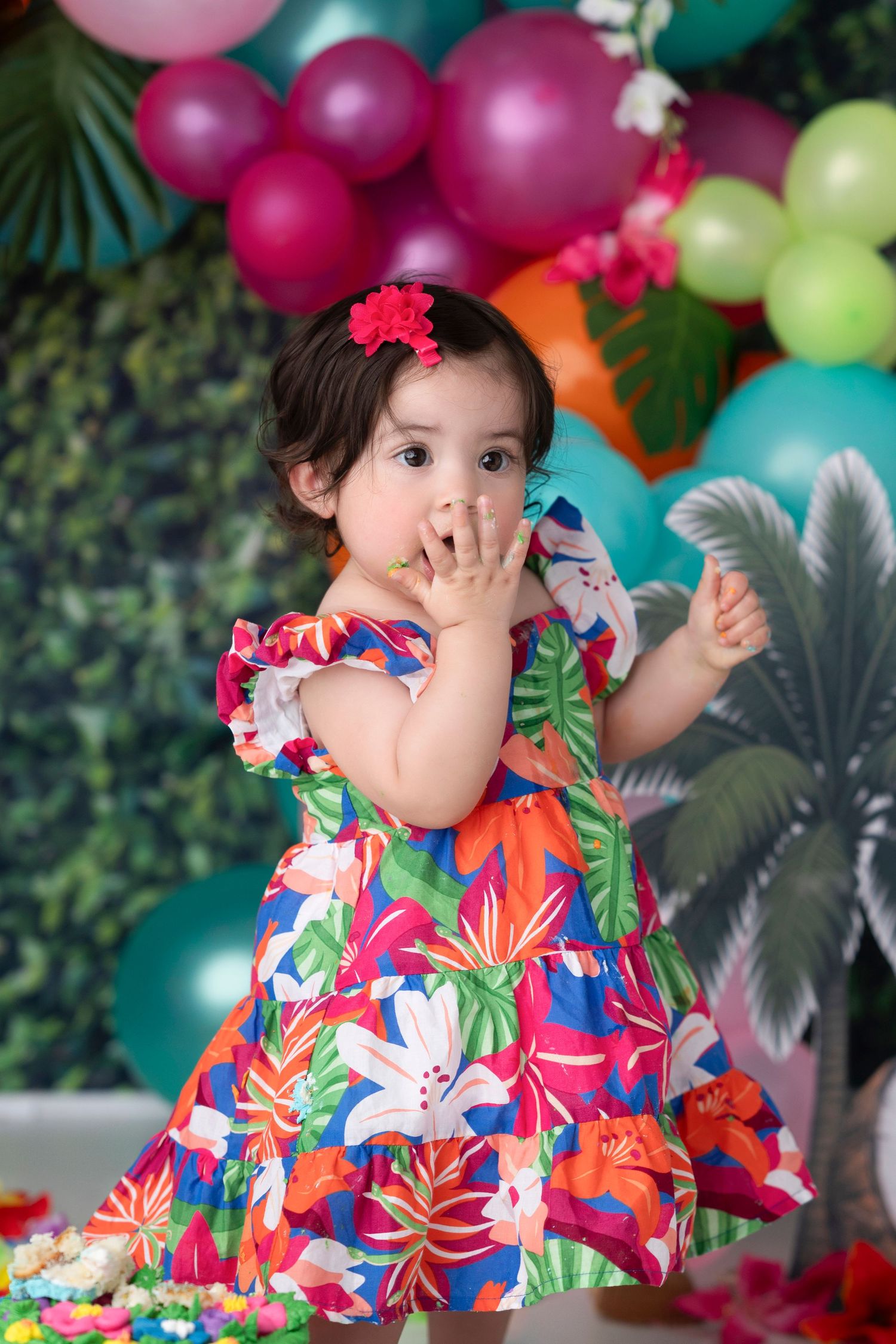 Colorful balloon arch decorates a tropical themed party with pink, green, and blue balloons against a leafy backdrop.
