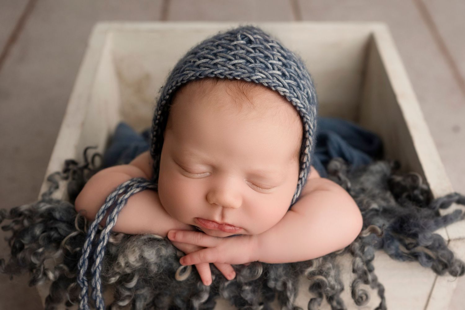 Peaceful sleeping newborn wearing a gray knit hat rests on soft textured gray fabric in artistic photography series.