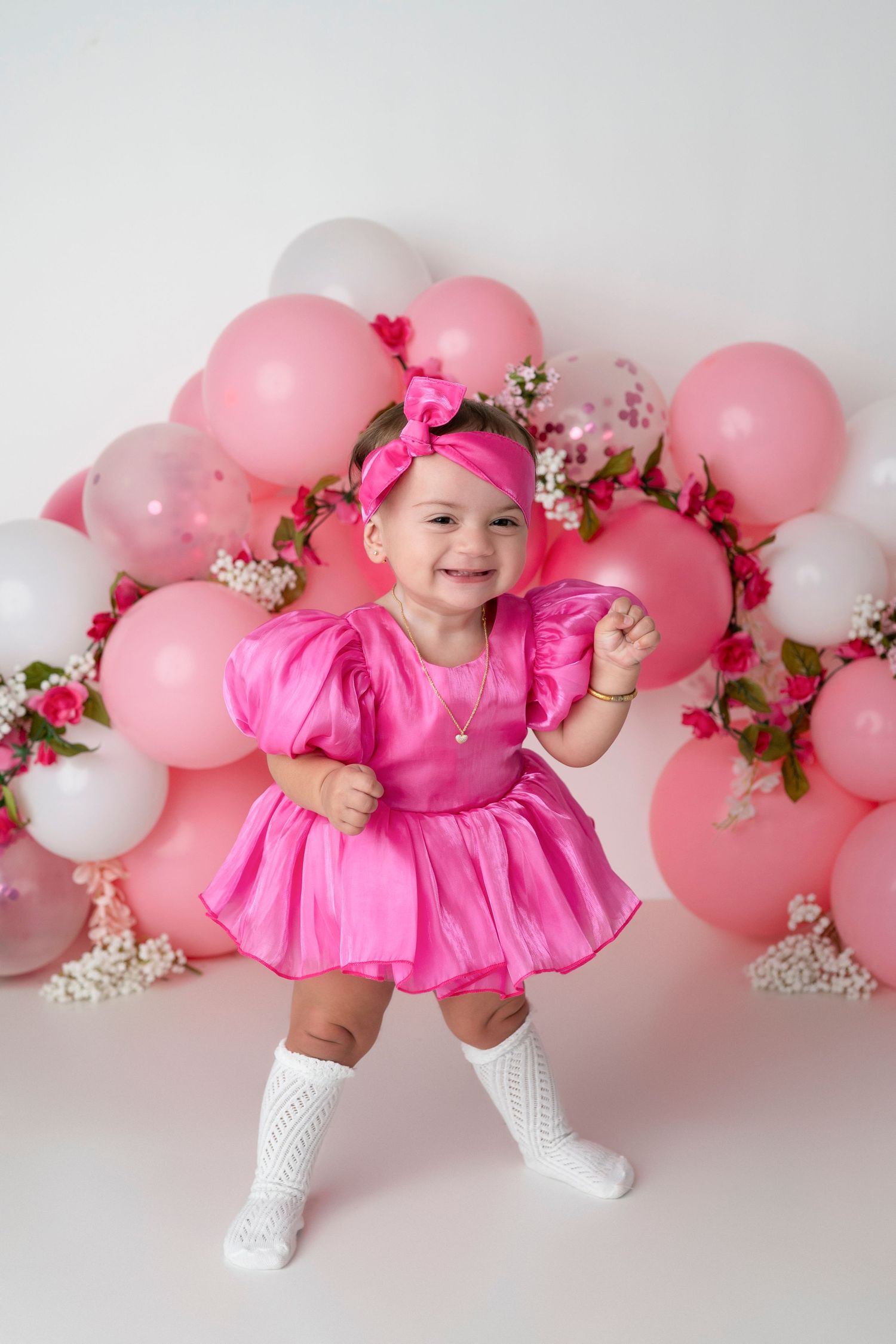 A series of photos with pink balloons and floral decorations arranged in a festive arch against a light background.