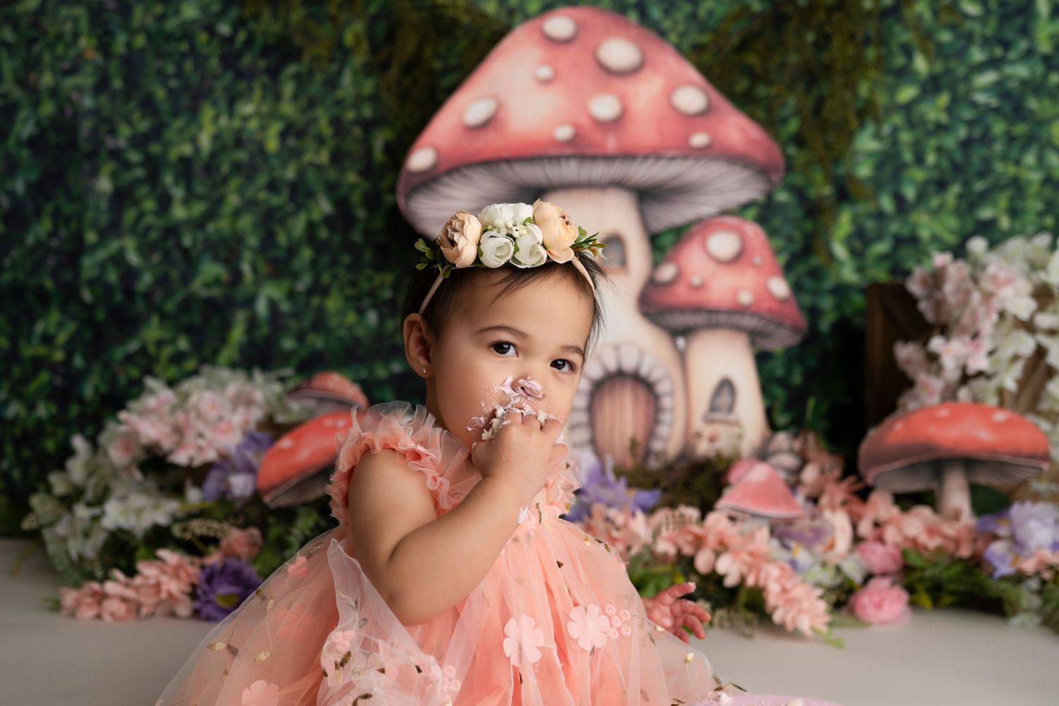 A magical fairy garden themed photoshoot setup with pink mushroom houses and floral decorations.