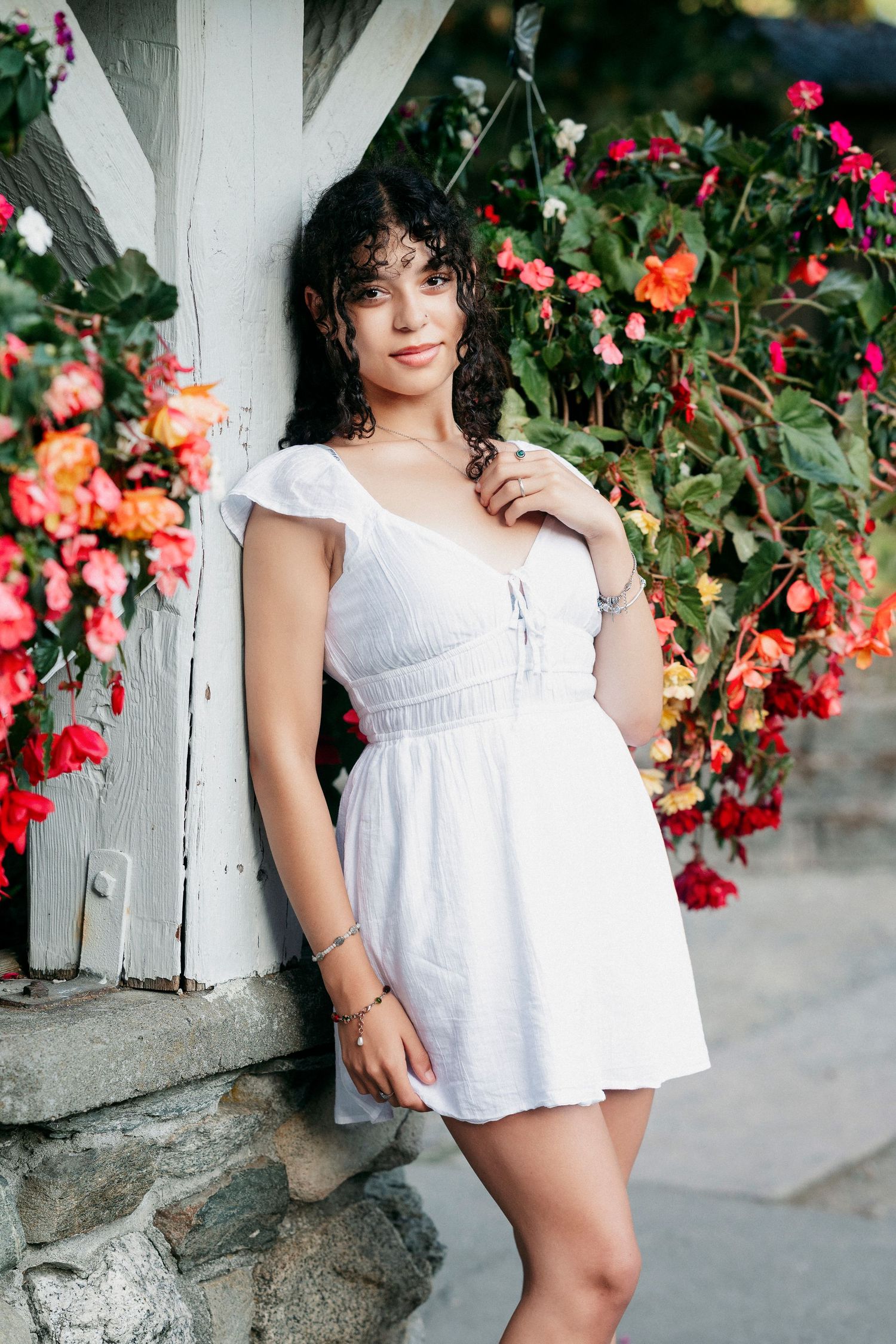A series of outdoor portraits in white summer dress against a wall with vibrant pink and orange flowering vines.