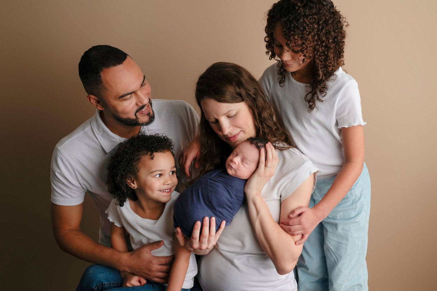 Family of five posing together, parents with three children including a newborn baby wrapped in blue cloth.