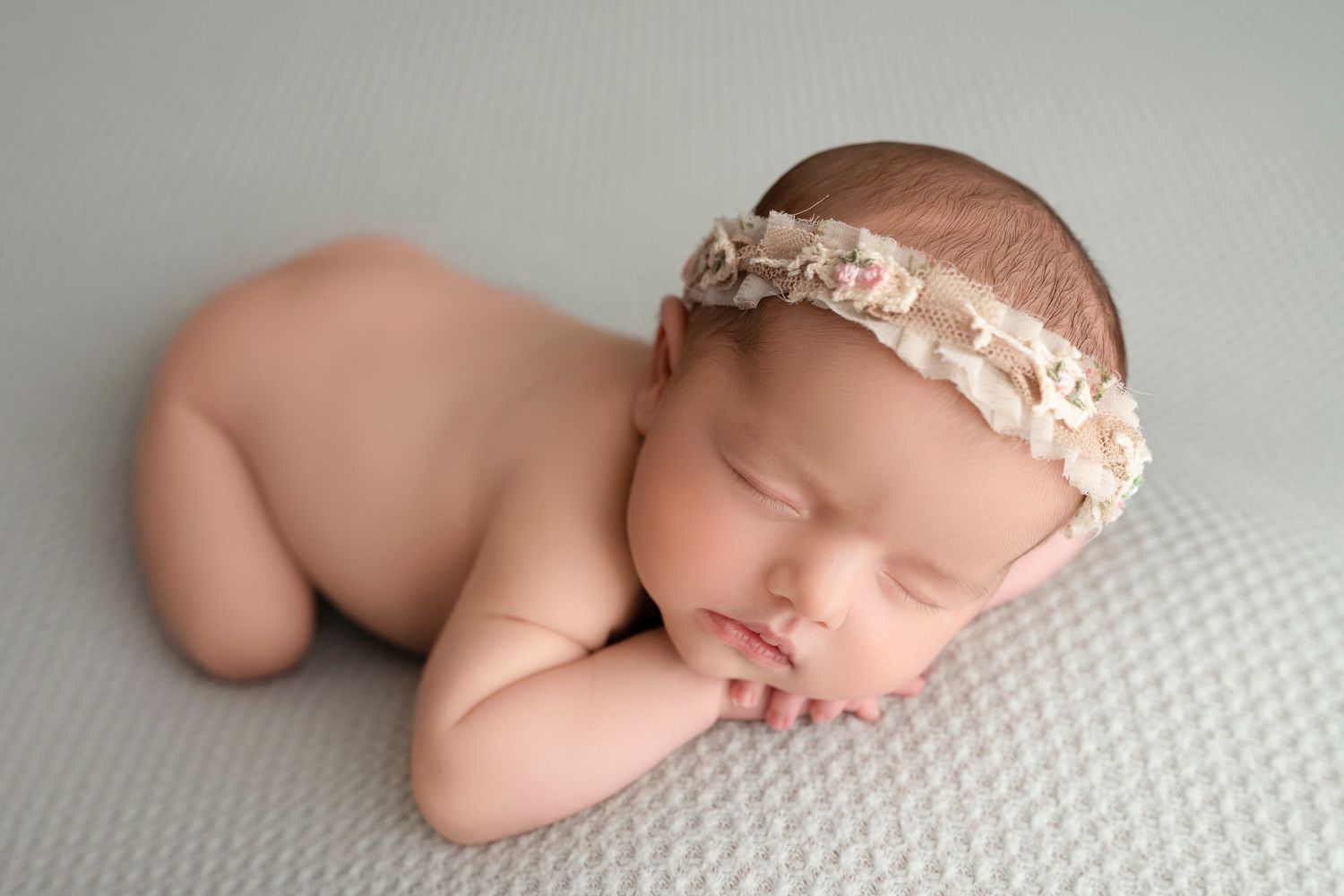 Sleeping newborn in delicate pink lace headband resting on white textured surface.