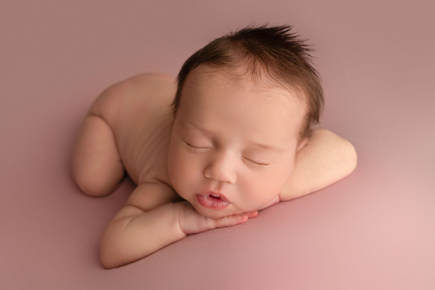 Peaceful sleeping newborn baby resting on soft pink background during professional photography session.