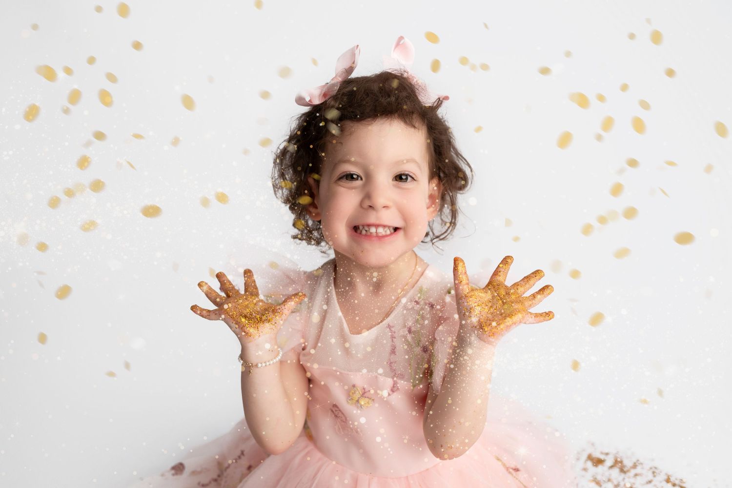 Child in pink dress plays with gold glitter confetti during joyful photo session.