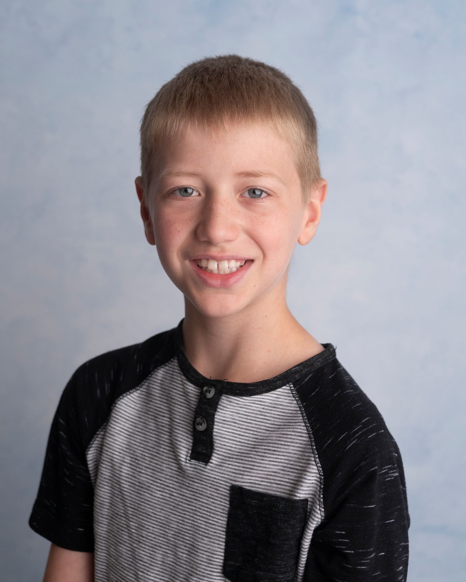 Young student poses for school photo wearing a casual black and grey henley t-shirt against a blue backdrop.