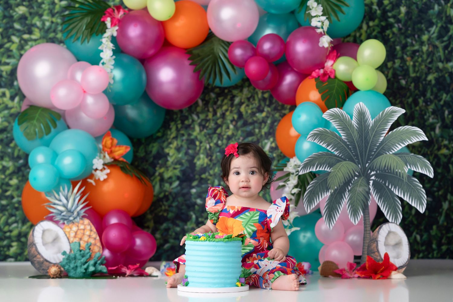 Colorful balloon arch with tropical decorations and silver palm trees creates a festive two-ican party theme backdrop.