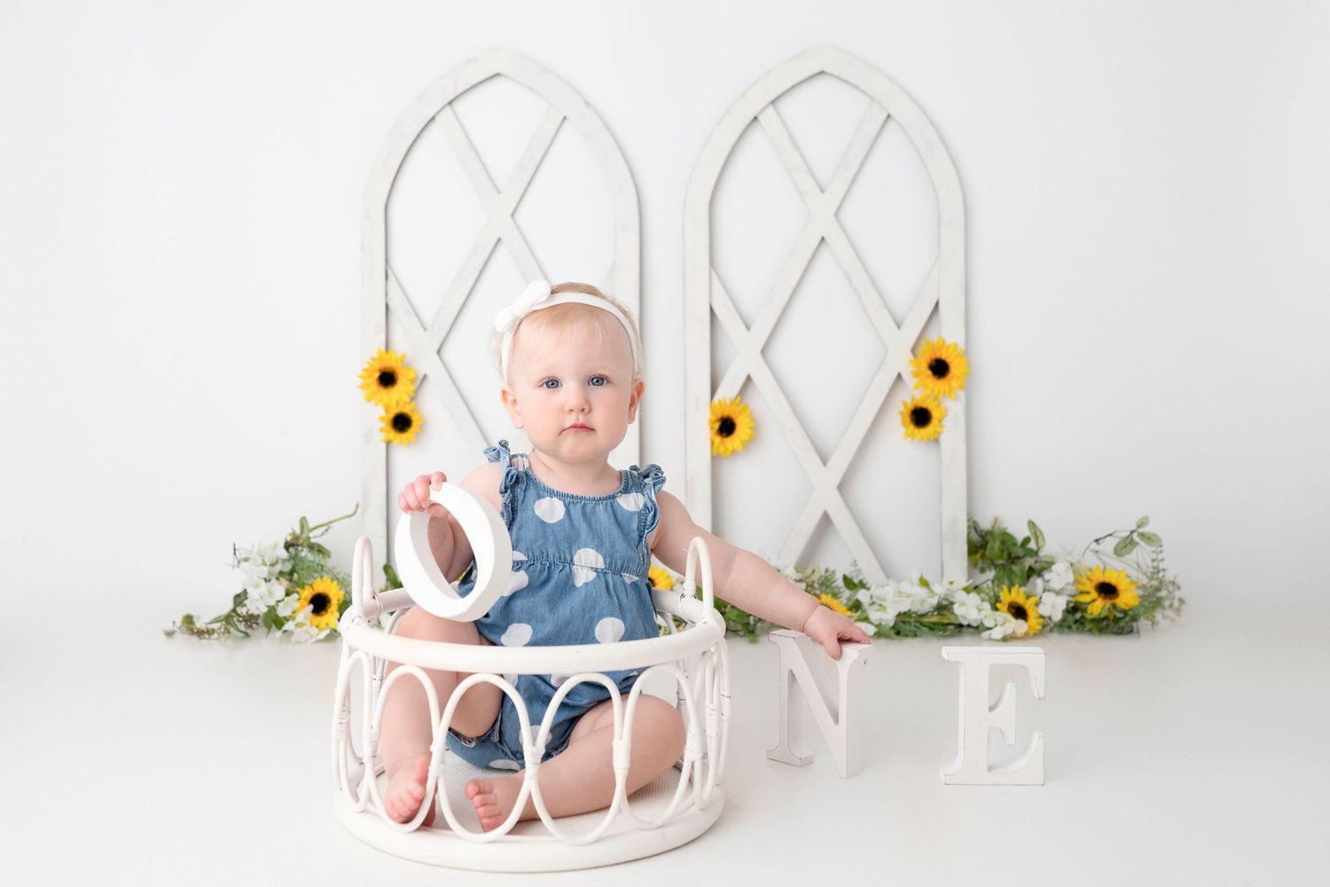 A white cake smash photography setup with sunflowers and lattice backdrop for a baby's first birthday session.
