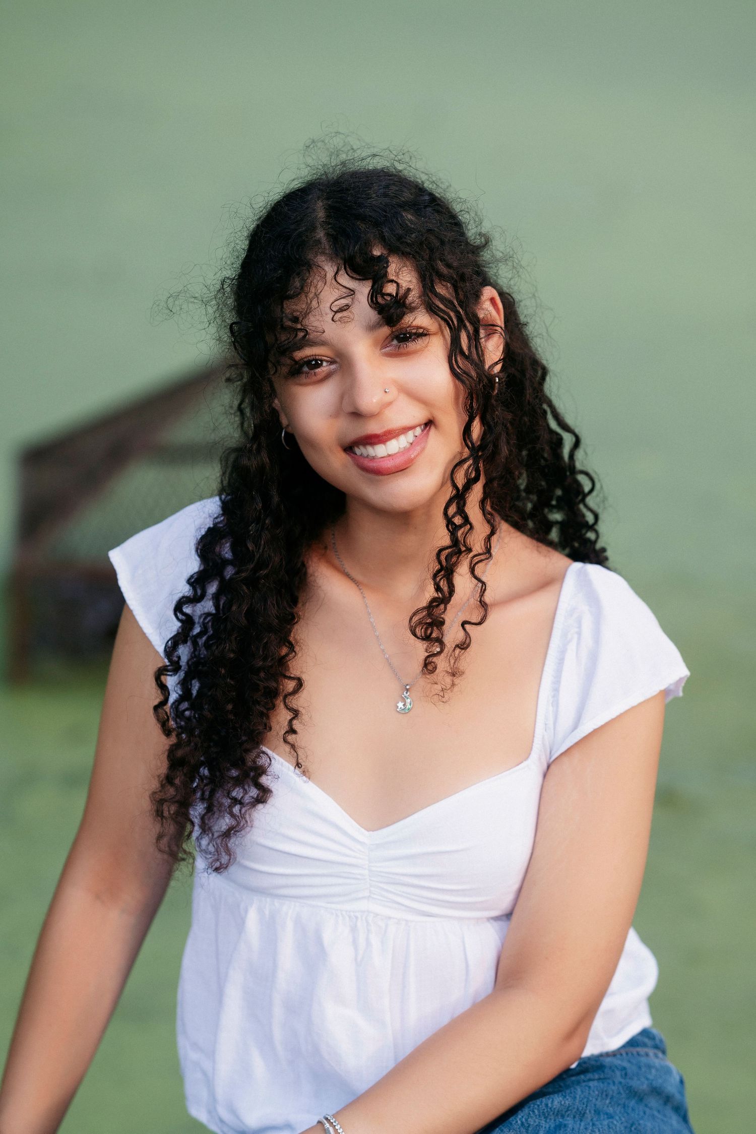 A person with curly dark hair wearing a white top and denim smiles warmly in a series of outdoor portrait shots.