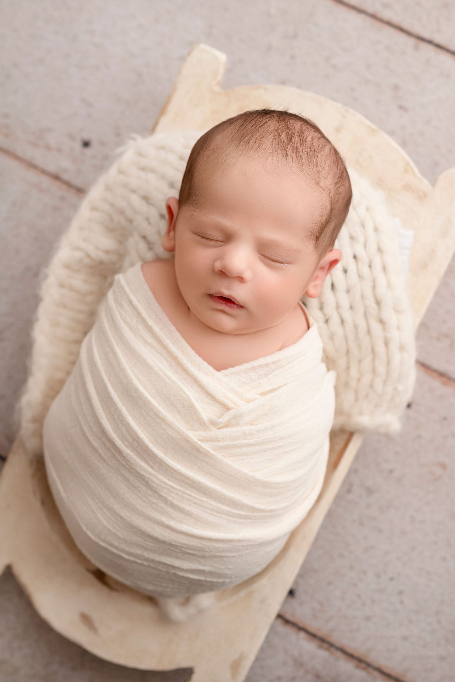 A sleeping newborn baby wrapped in soft white fabric is photographed from different angles in a studio setting.