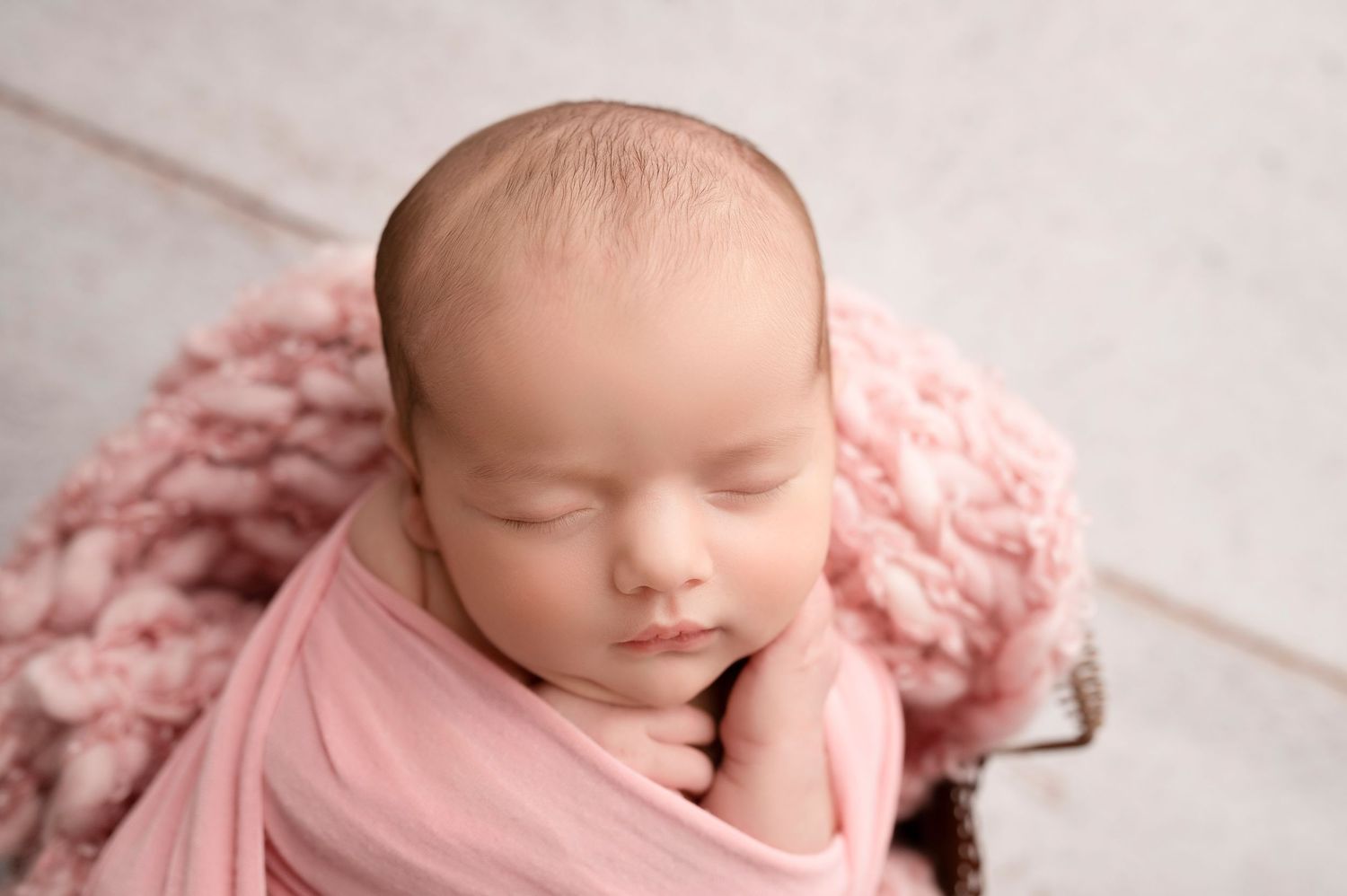Sleeping newborn swaddled in soft pink blanket during professional photography session.