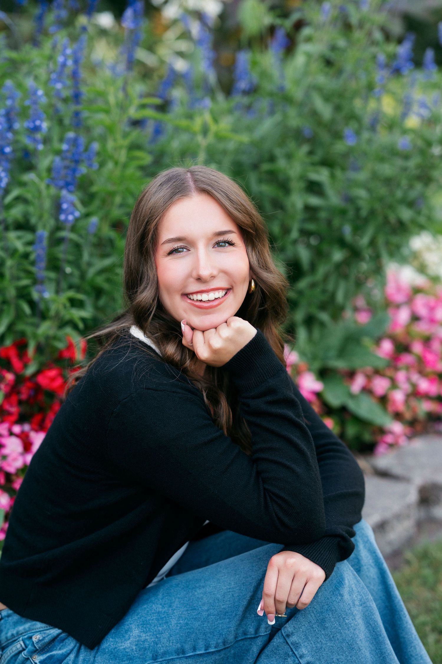 A series of casual portrait poses in a black sweater against a colorful garden backdrop with delphiniums.