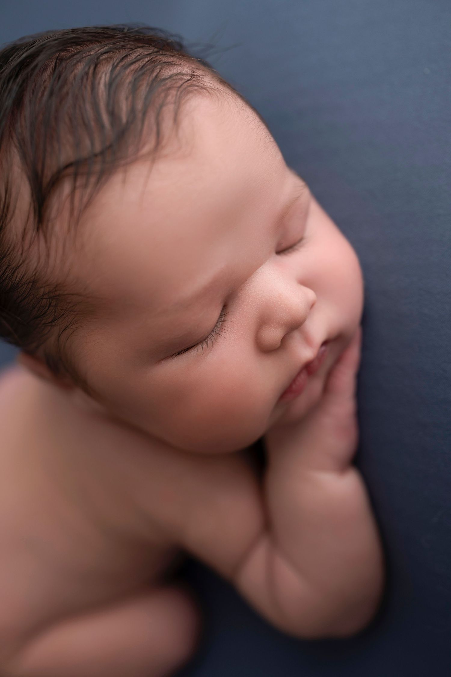 A sleeping baby rests peacefully against a dark blue background in a series of gentle profile portraits.