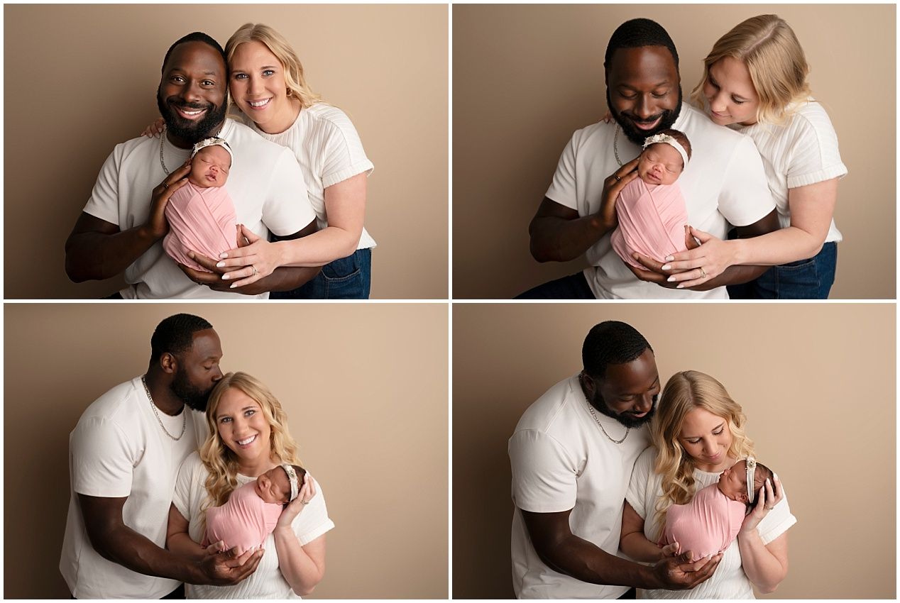 Interracial couple in white shirts tenderly holding their newborn wrapped in pink during a studio portrait session.