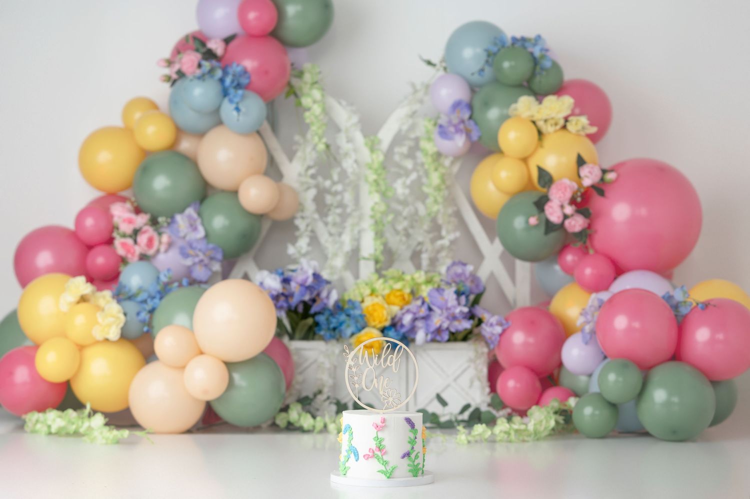 Pastel balloon arch display with butterfly decor and floral arrangements in soft spring colors against white backdrop.