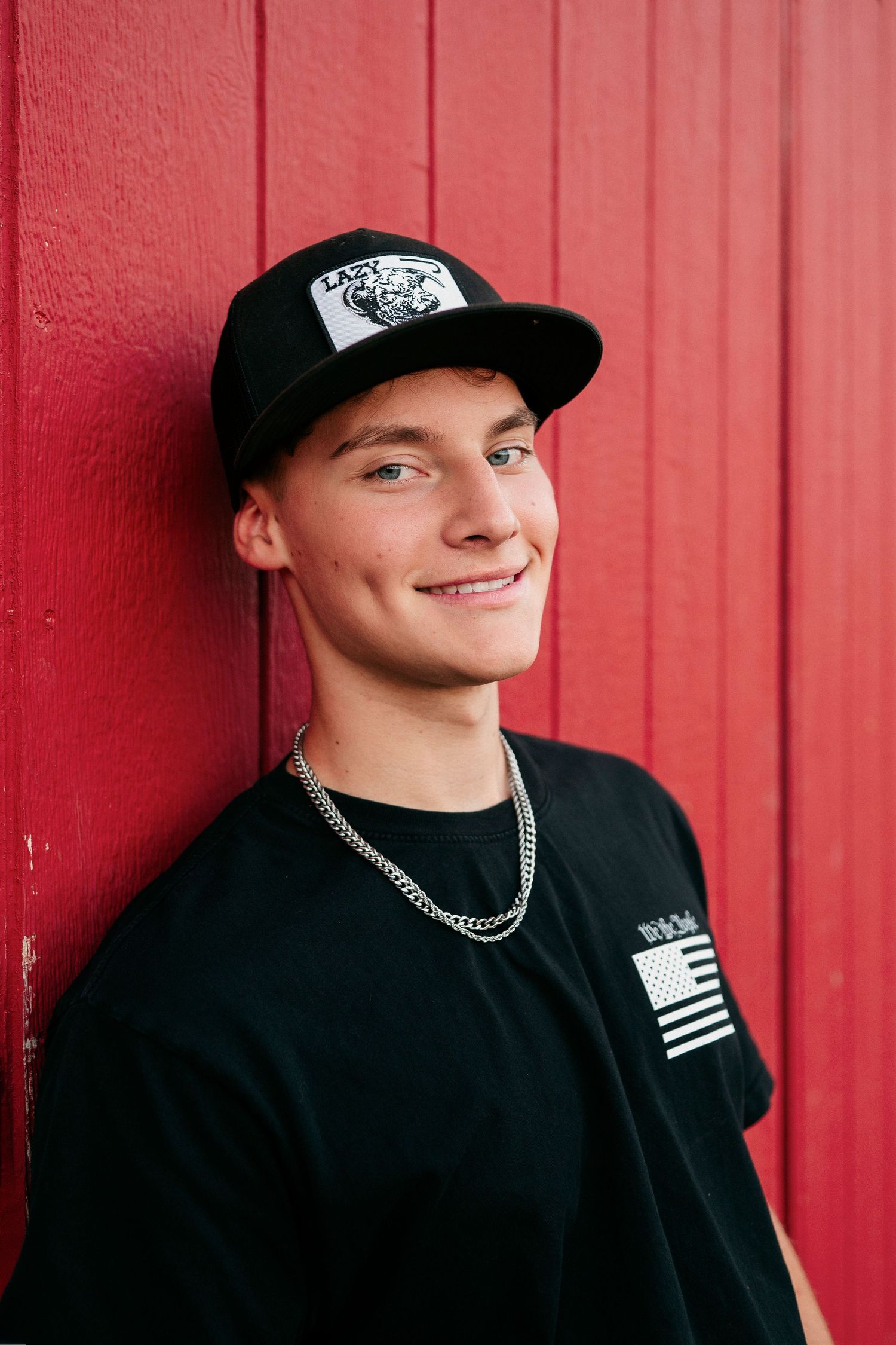 A person wearing a black baseball cap and shirt poses against a bright red wall in a series of casual portraits.
