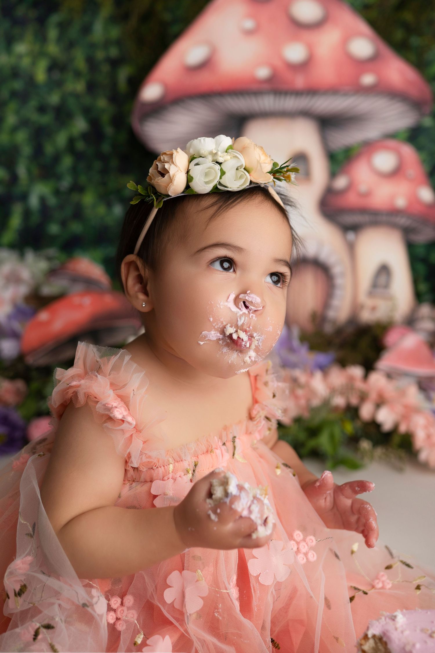 Whimsical fairy tale photo with pink dress, floral crown and painted mushroom backdrop in enchanted garden setting.