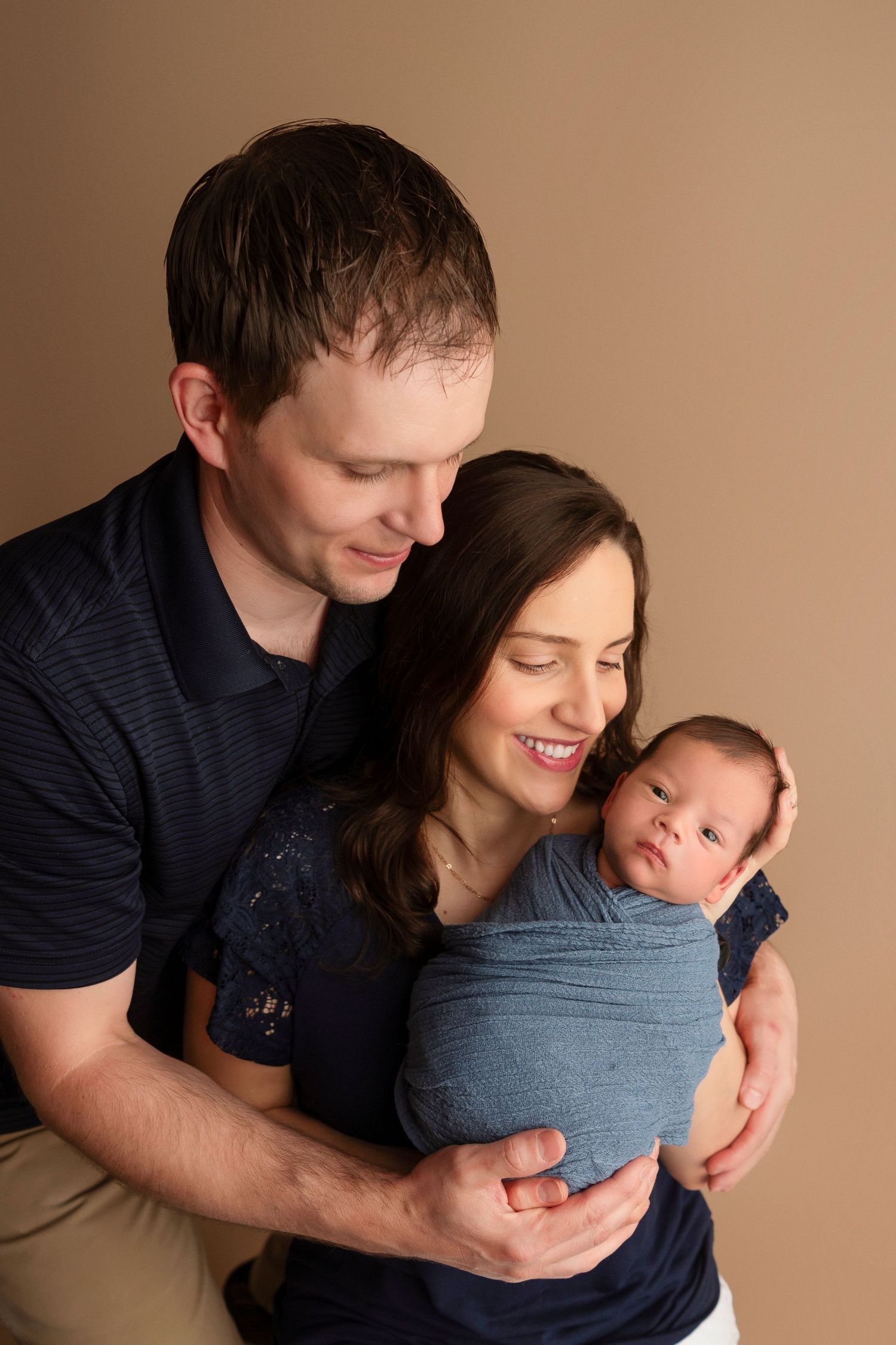 A series of tender moments between parents and their newborn baby wrapped in blue fabric against a neutral backdrop.