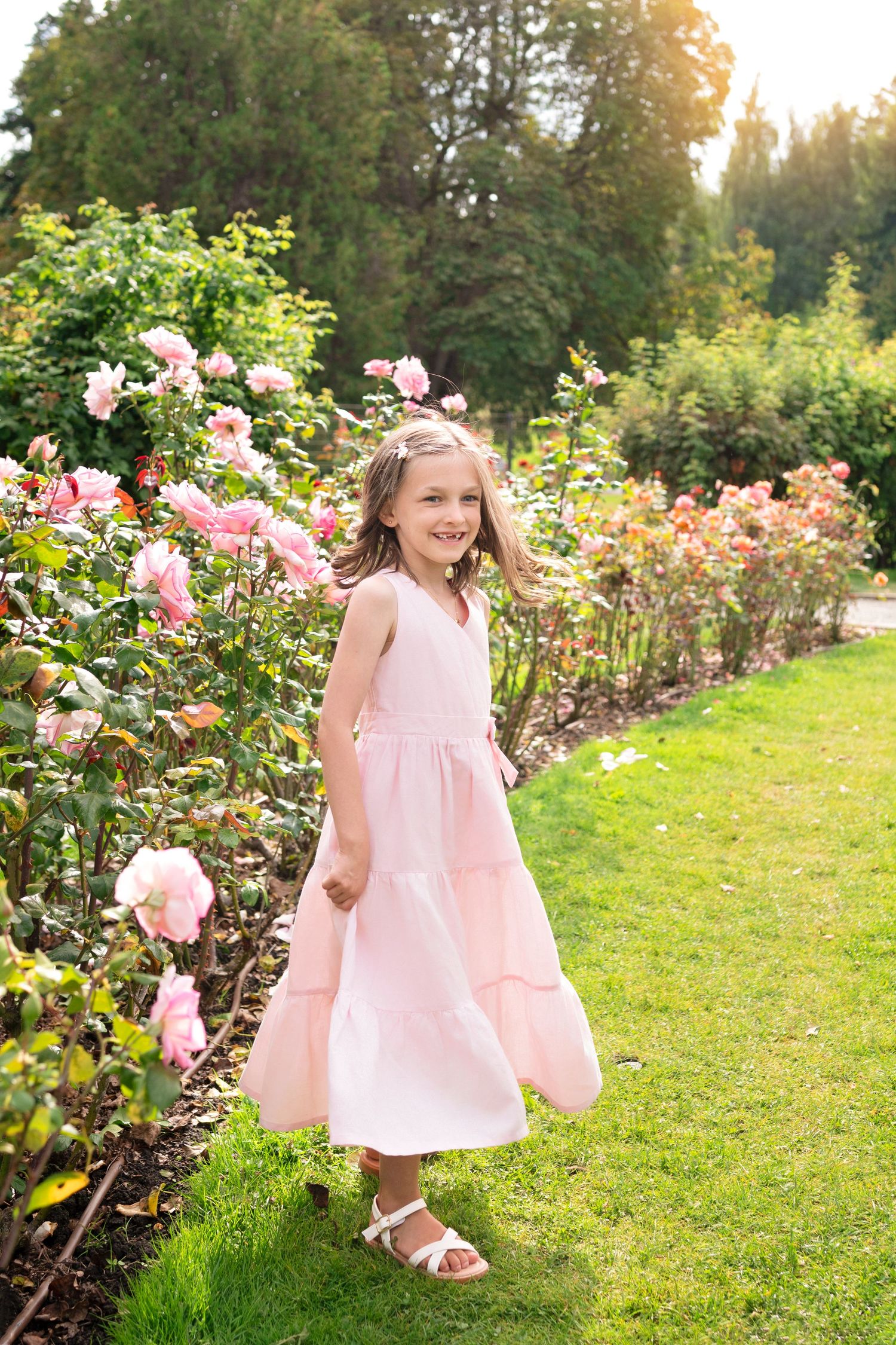 A child in a pink dress plays in a garden with blooming roses during golden hour sunset.