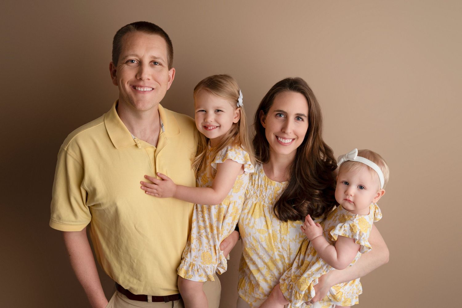 A family wearing coordinated yellow and beige outfits poses together for a series of professional portraits.
