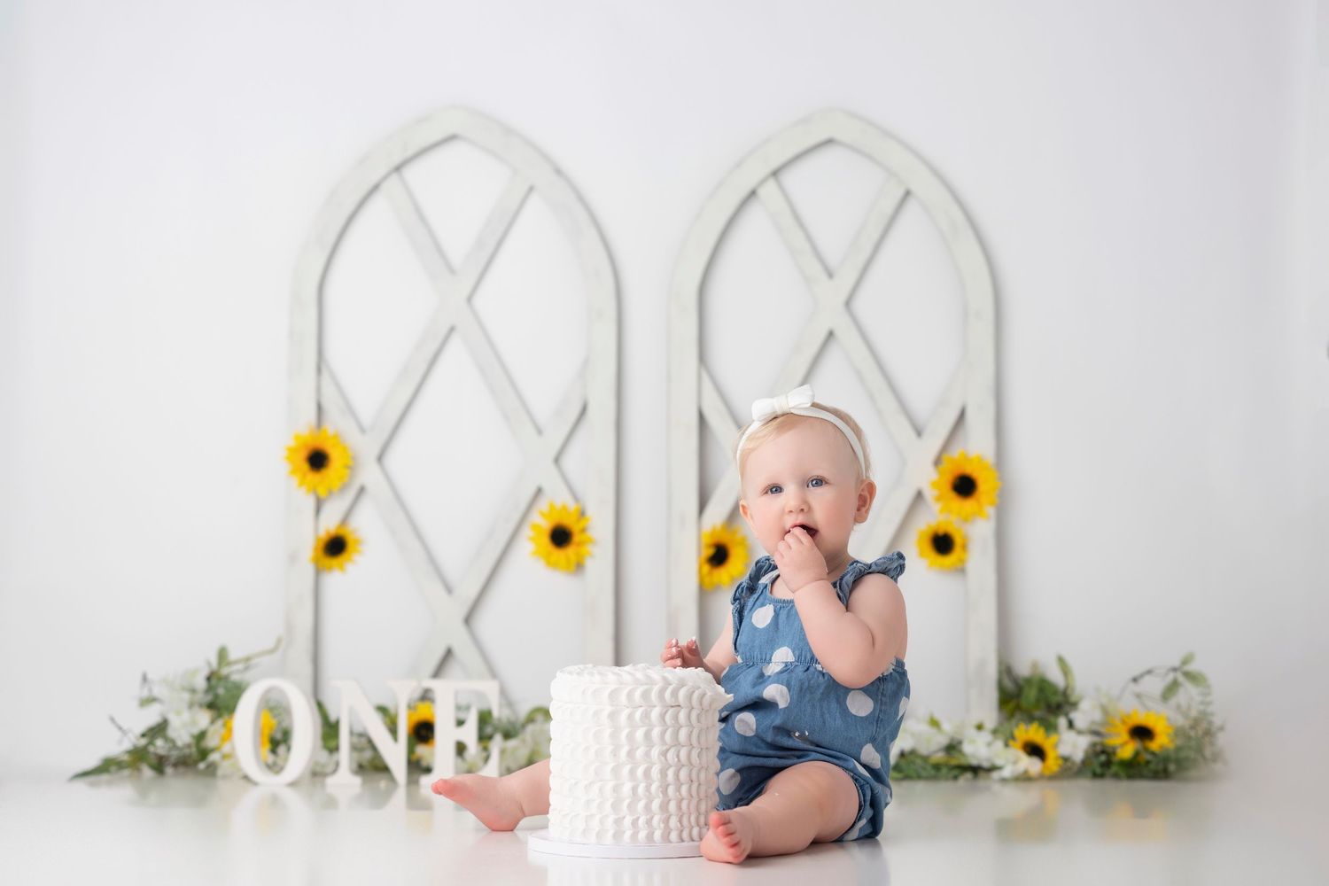 A white headboard backdrop with yellow sunflowers creates a bright and cheerful setting for a baby photography session.