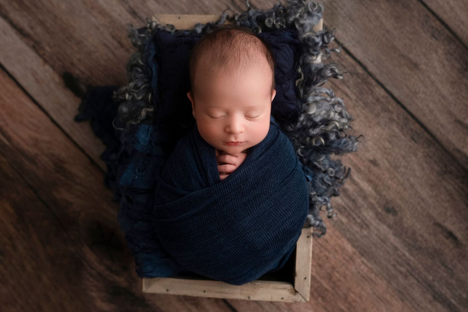 Sleeping newborn on dark wood backdrop with navy blue accents in artistic portrait style.