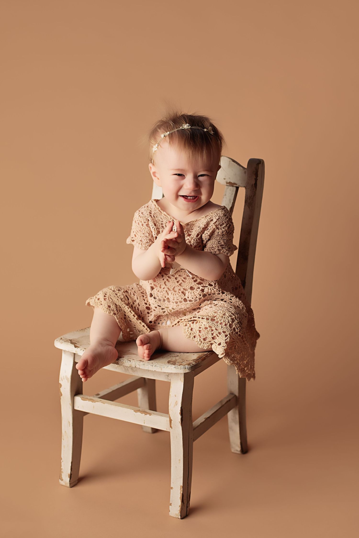 Five sequential photos show a baby in peach-colored lace dress sitting and playing on a small distressed white wooden chair.