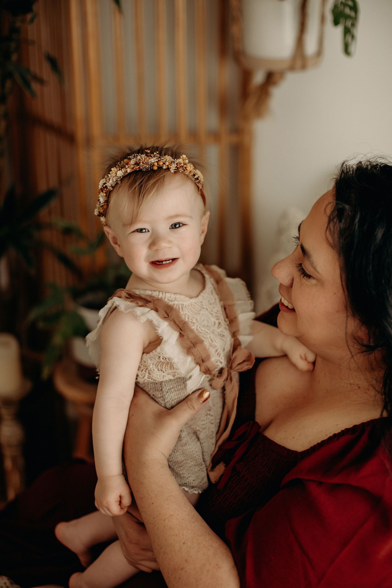 Parent in red sweater lovingly holding and interacting with a baby wearing delicate lace dress.