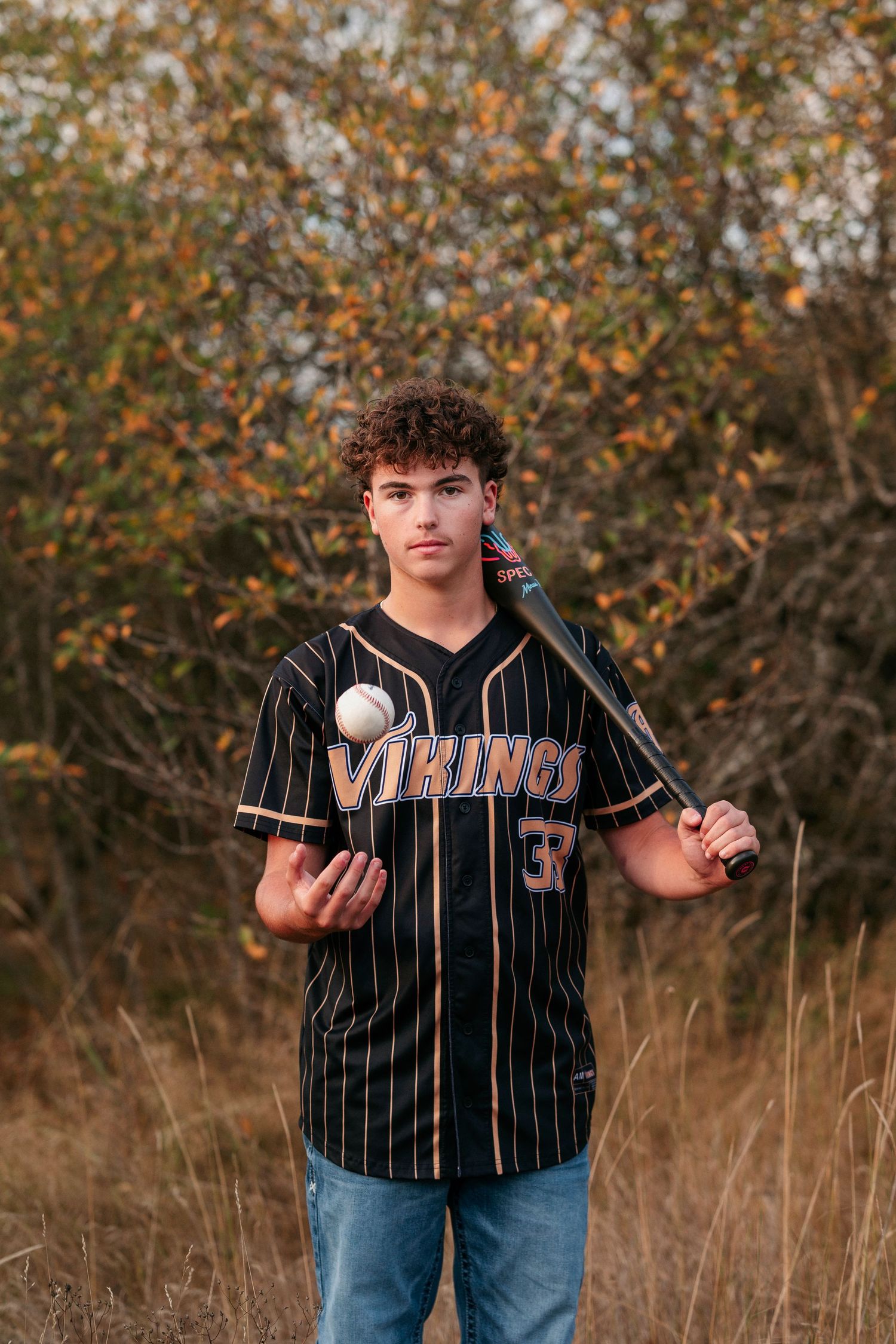 Baseball player in Vikings pinstripe jersey demonstrates ball handling techniques in autumn field setting.