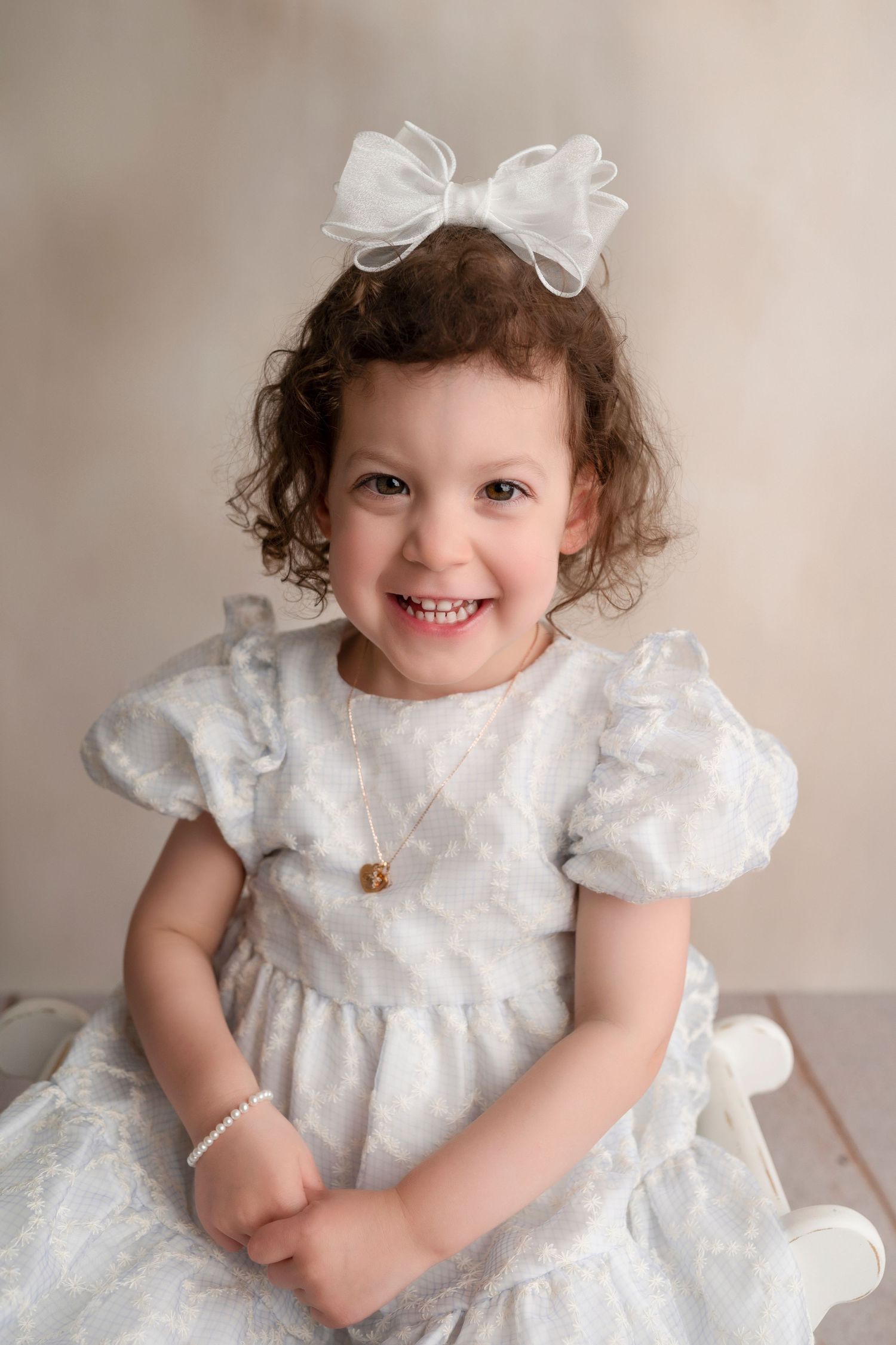 A white lace dress with puff sleeves and pearl accessories creates an elegant portrait setting.