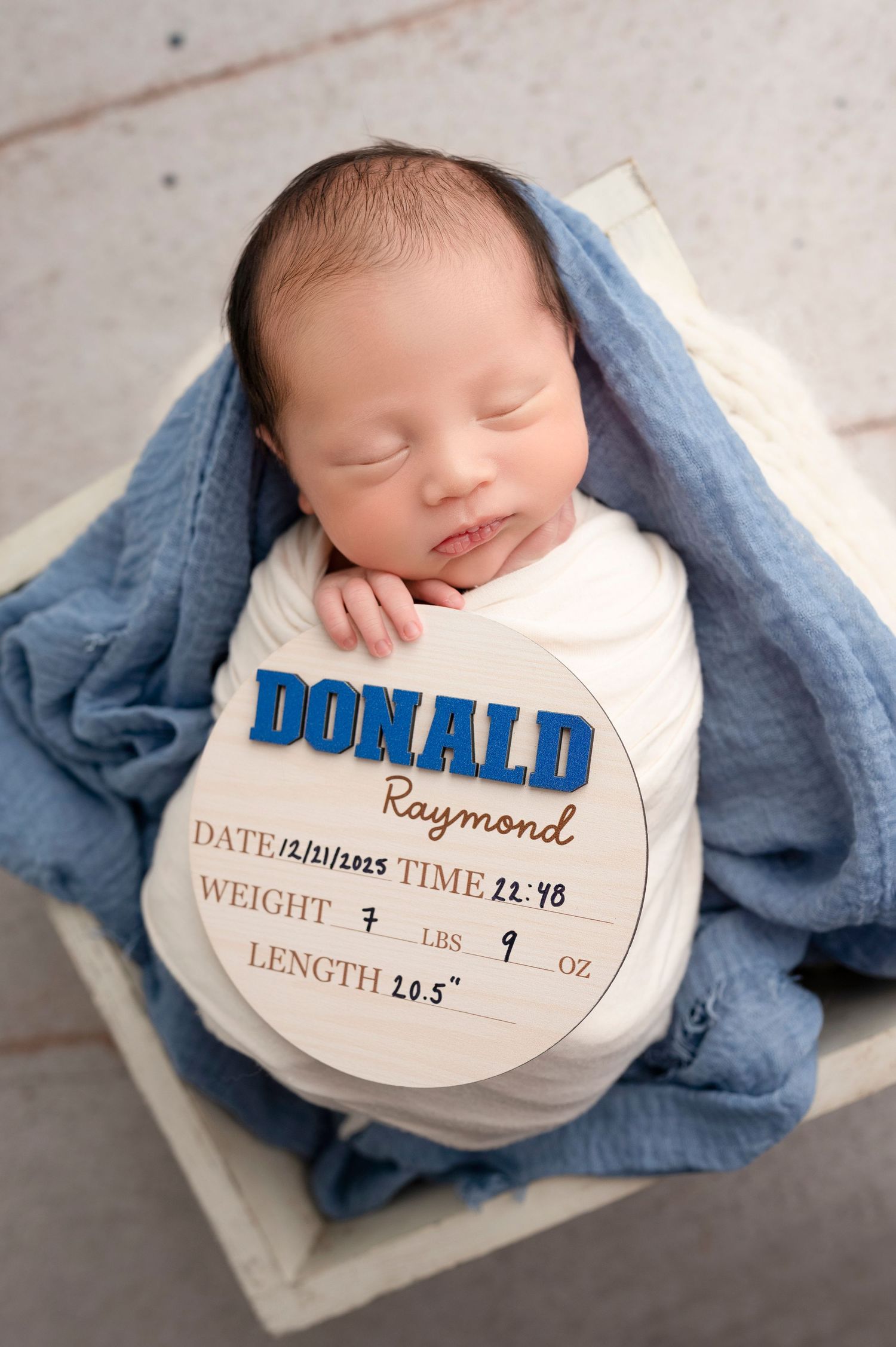 Newborn baby Donald Raymond sleeping in a white wooden box with a blue wrap and birth stats sign showing 7lbs 9oz.