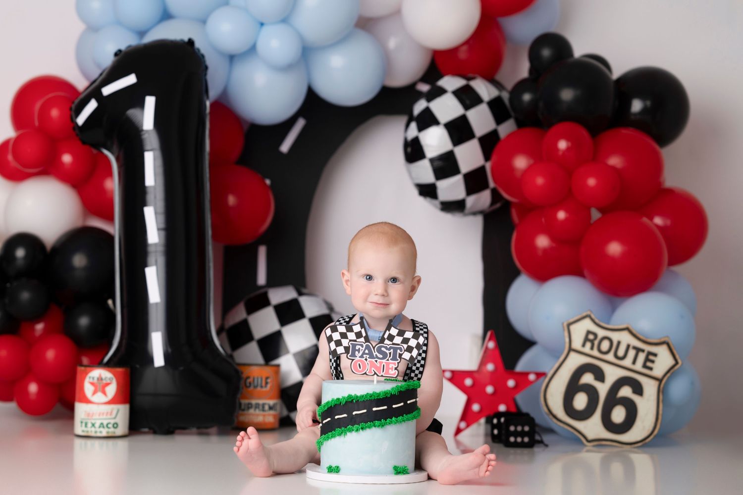Baby's first birthday cake smash with Route 66 racing theme, balloons, and number one decorations.