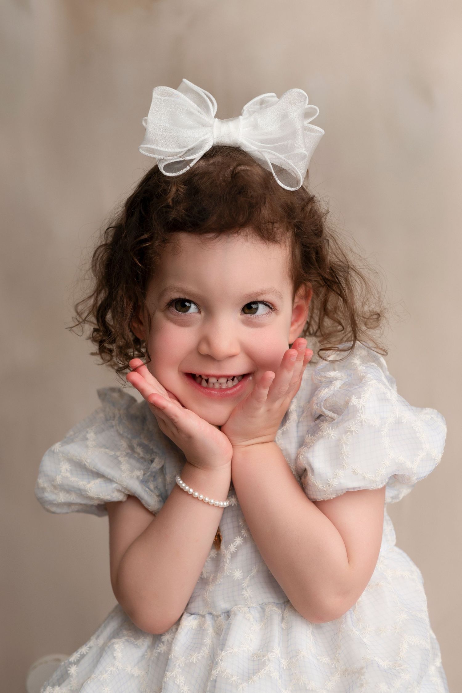 A white formal dress with delicate lace details and a matching bow creates a charming portrait setting.