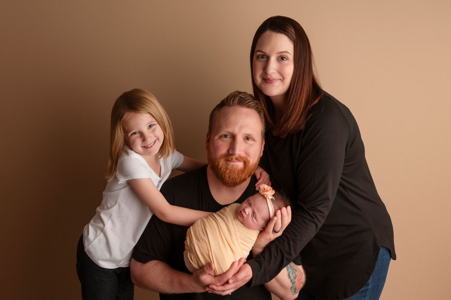 A family poses together in a warm-toned studio setting wearing coordinated black and white outfits.