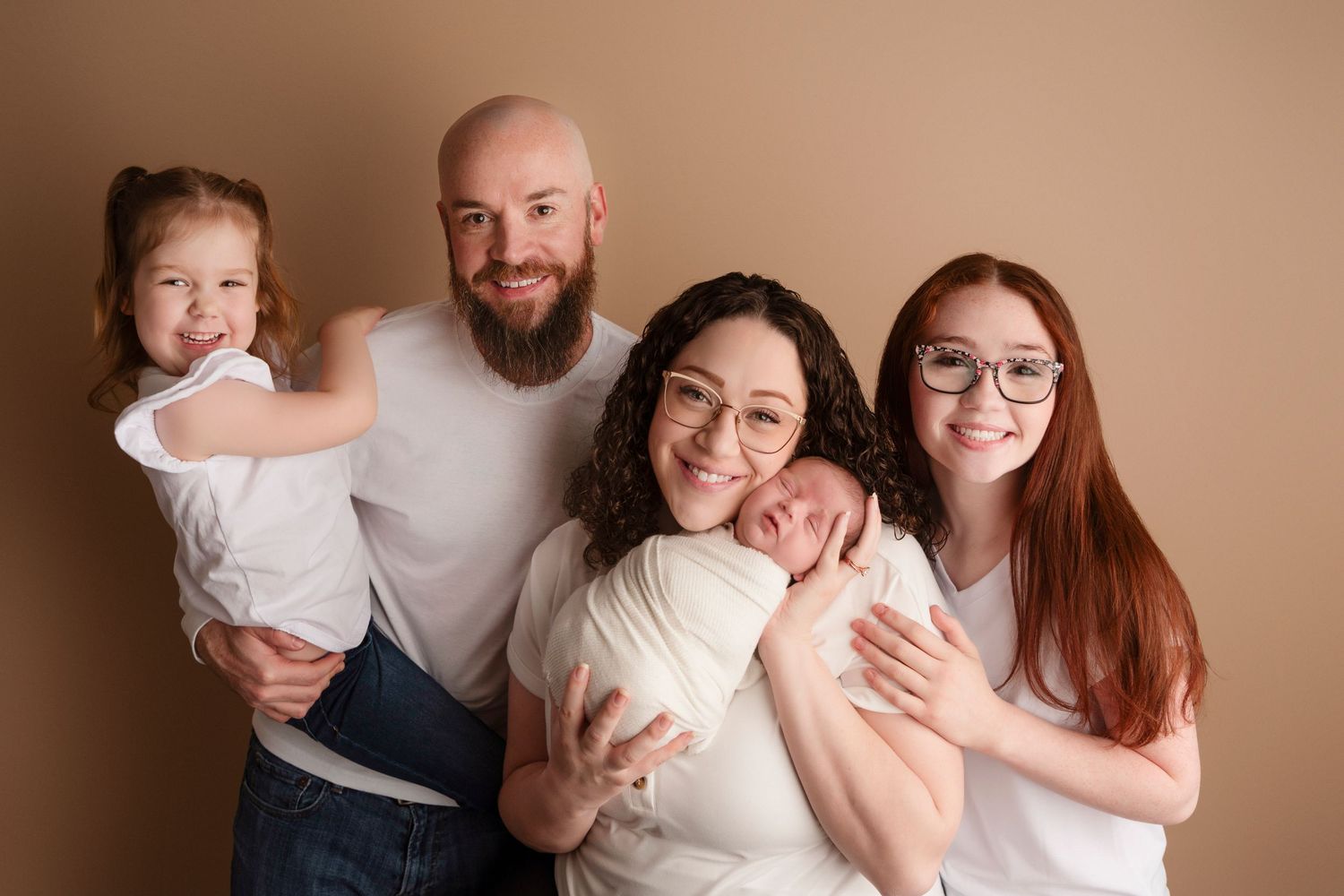 A family wearing coordinated white outfits embraces and laughs together during a warm-toned portrait session.
