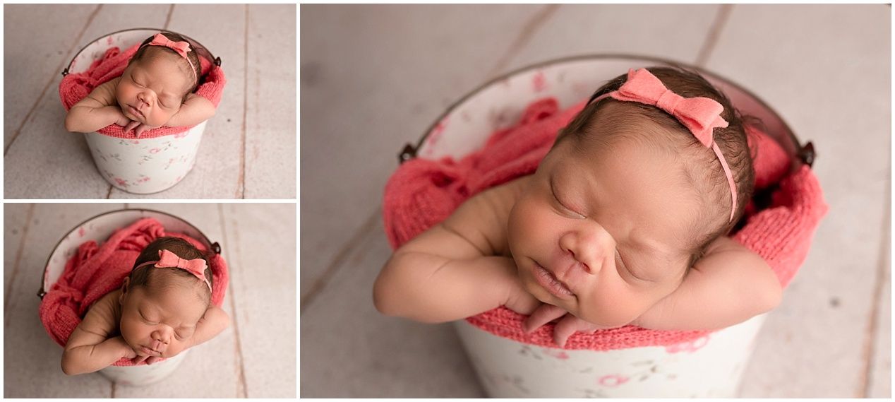 Sleeping newborn baby girl in pink bow headband curled up in white bucket with coral blanket for professional photo session.