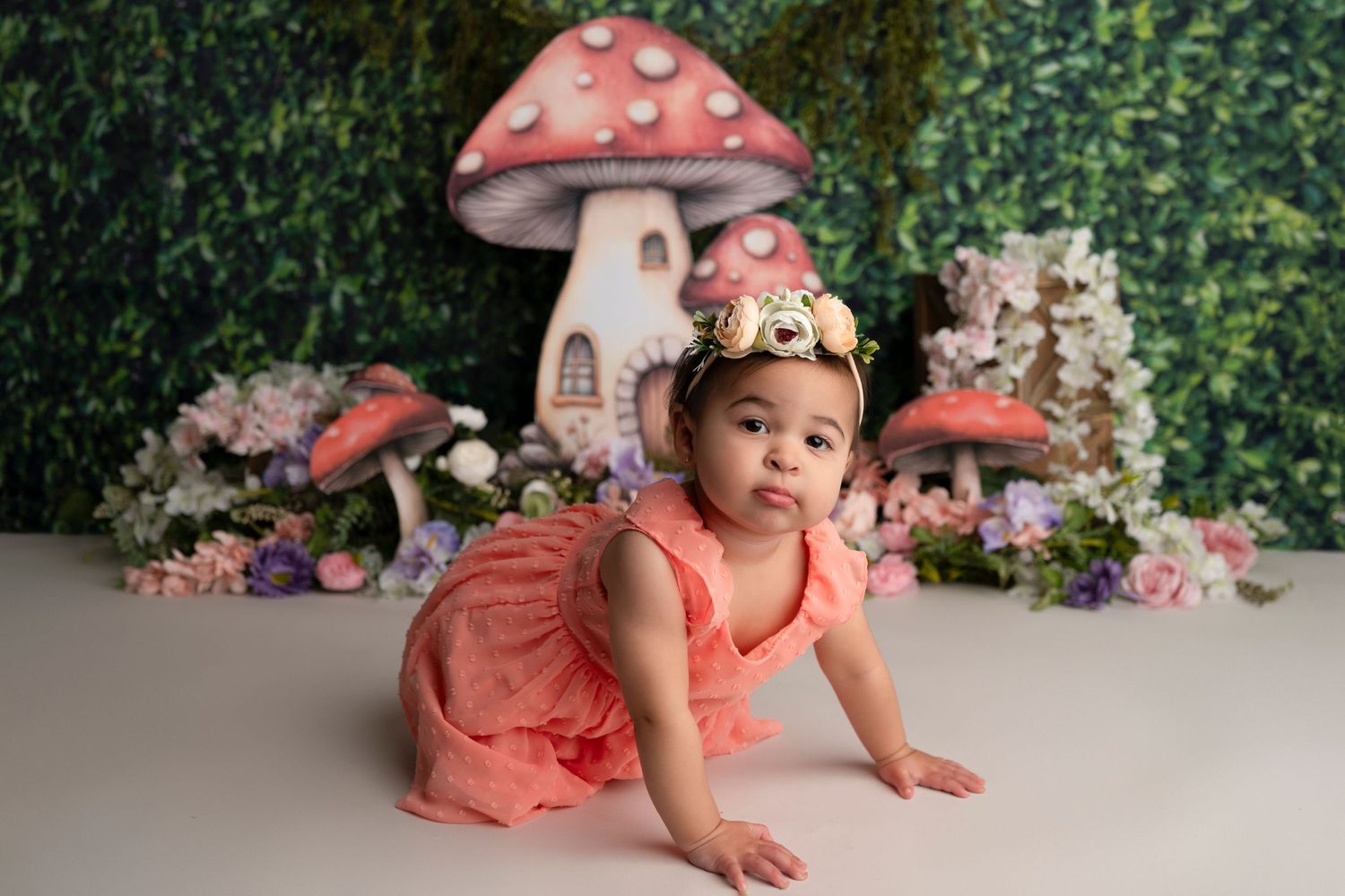 Charming photo series with coral dress and mushroom-themed props against green foliage background.