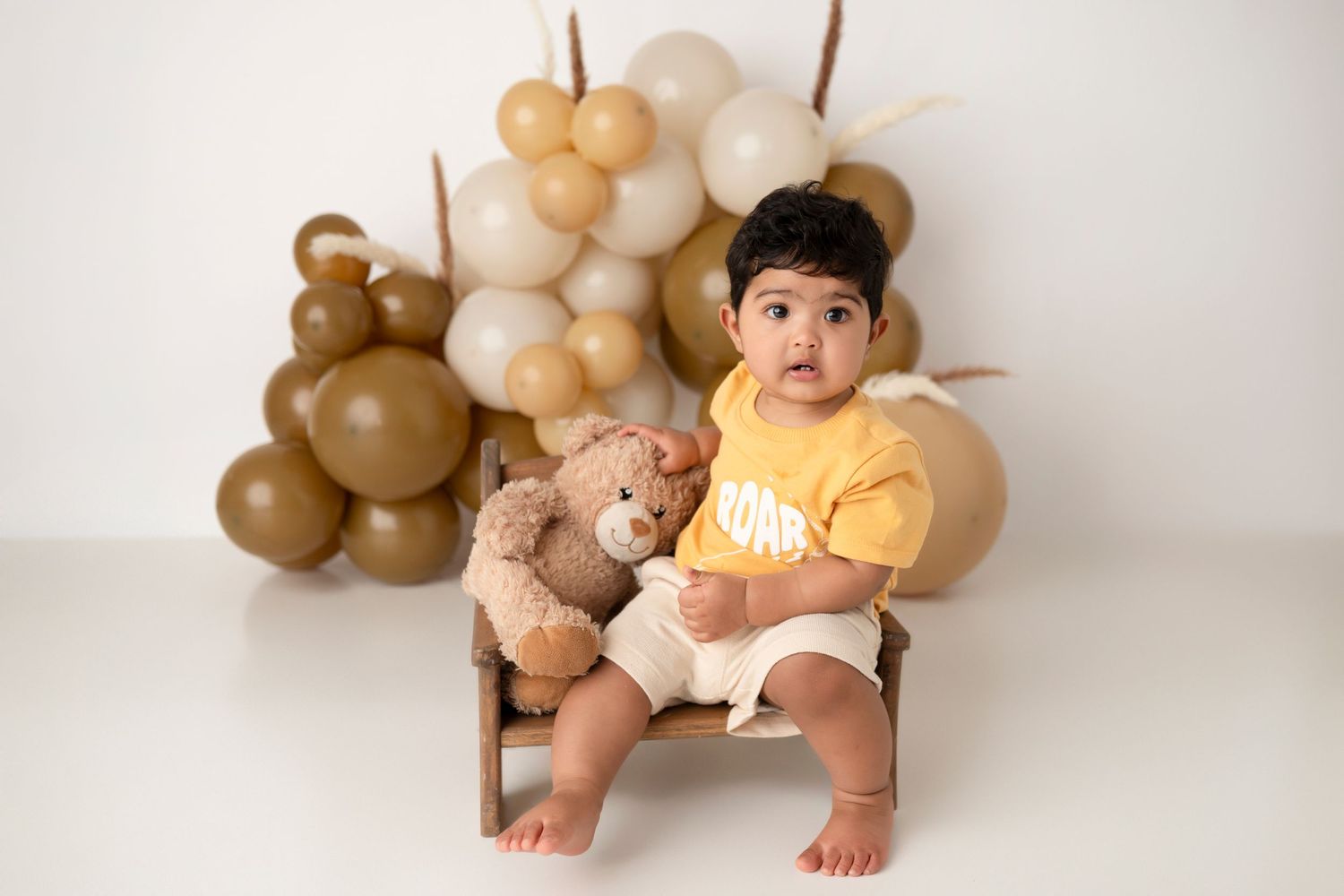 A baby milestone photo collage showing monthly growth with brown balloon decorations against a white backdrop.