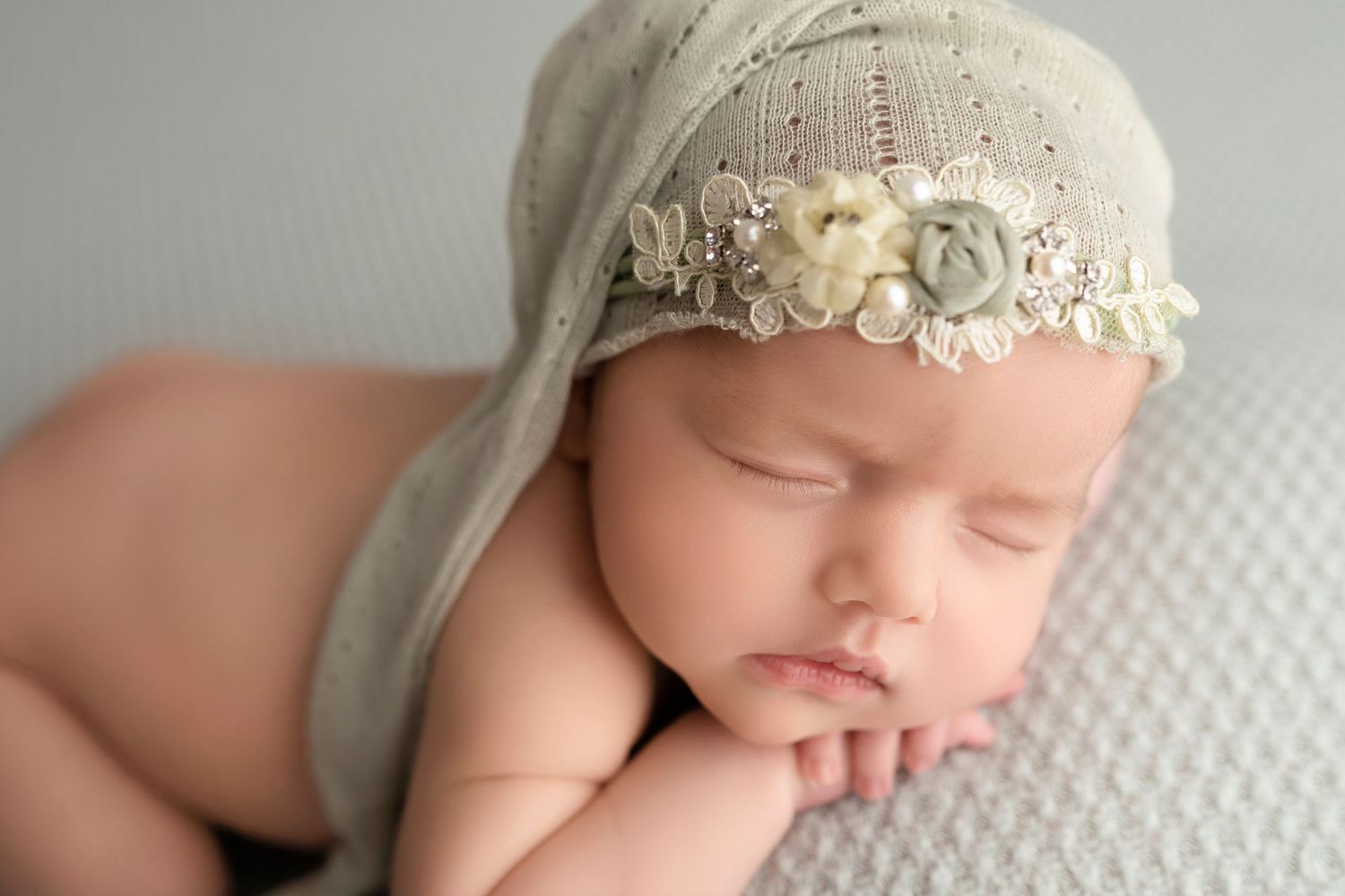Newborn resting peacefully with delicate lace headband during professional portrait session.