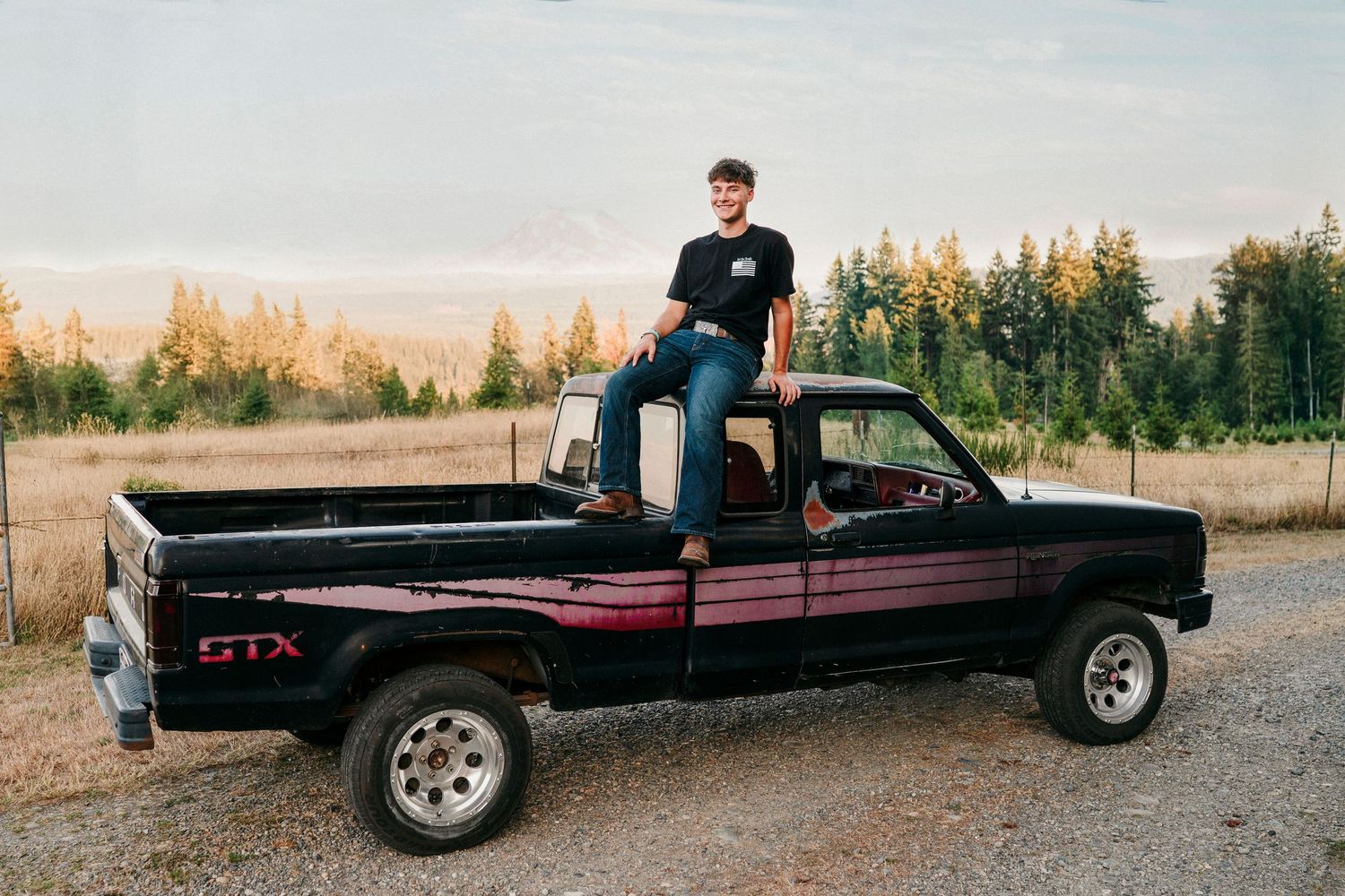 A black pickup truck parked in a rural field during golden hour with mountains and trees in the background.