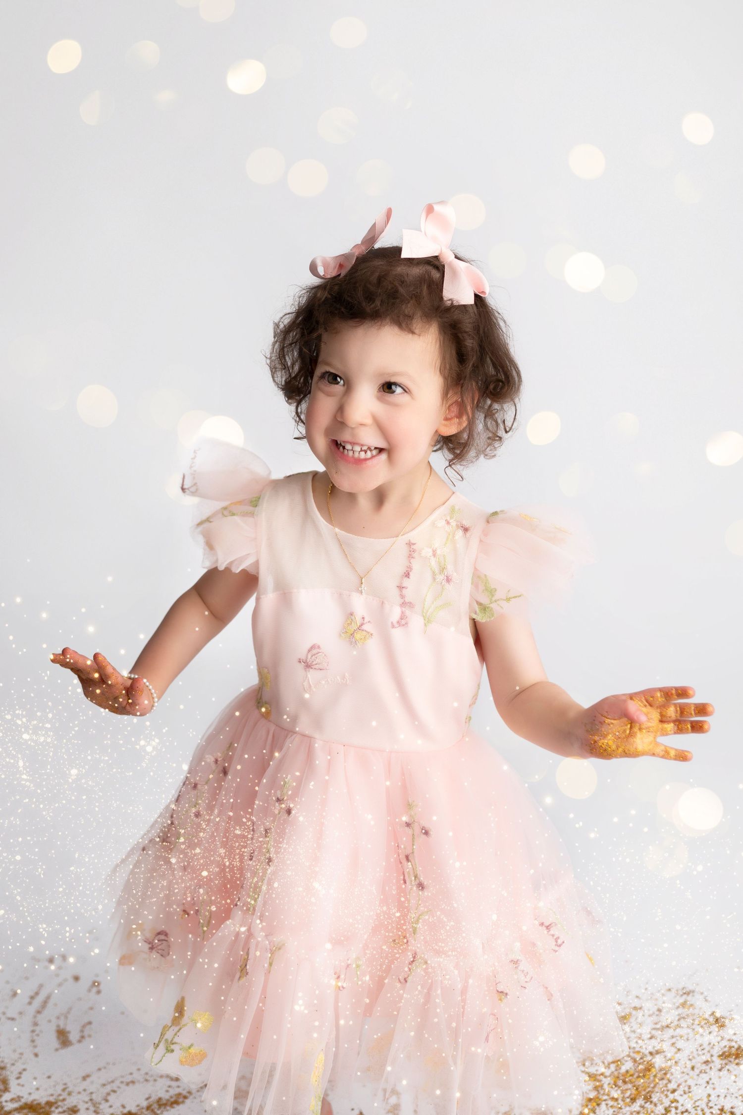 A joyful moment captured as a child in a pink dress plays with sparkly gold glitter against a white backdrop.