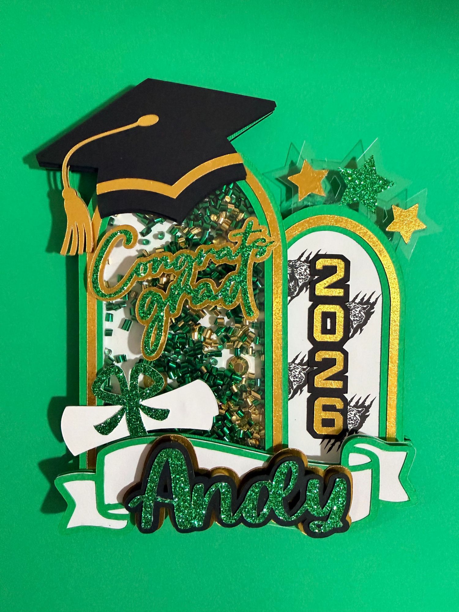 Personalized graduation cake topper for Andy, class of 2026, in green and gold glitter with mortarboard cap.