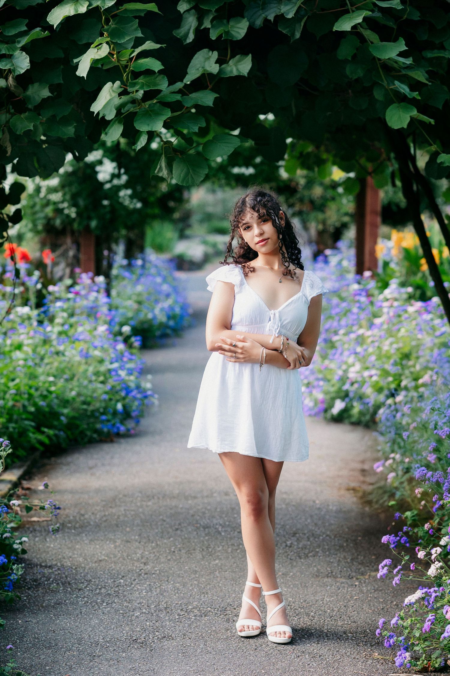 A path lined with purple wildflowers and green trees creates a serene garden setting for a summer photo session.