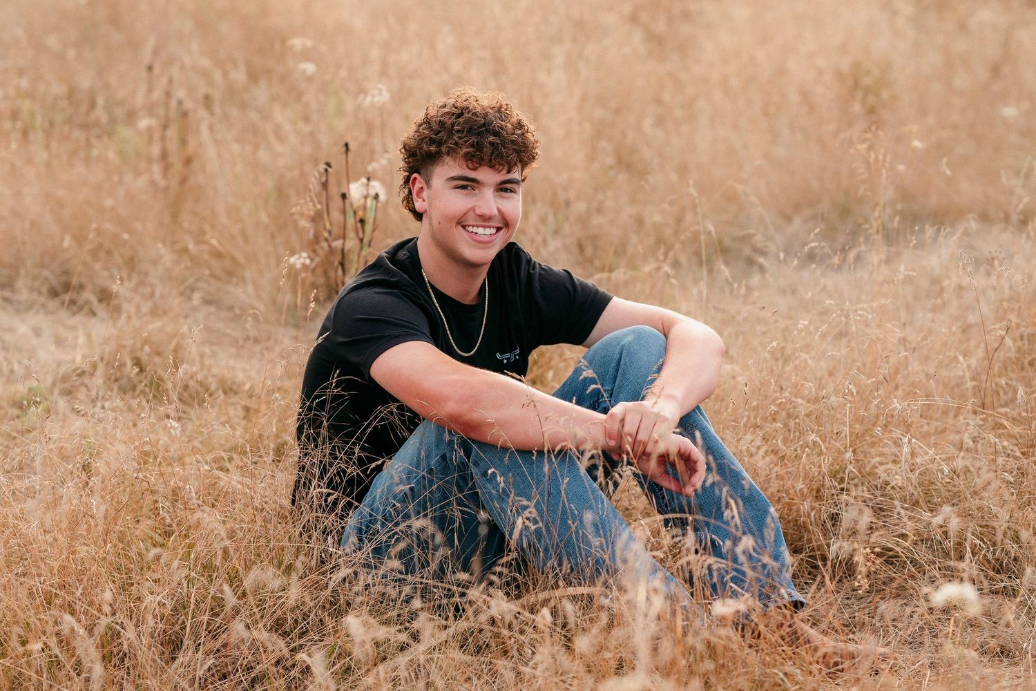 A person in a black shirt sits in a golden field during sunset creating a warm and peaceful outdoor portrait.