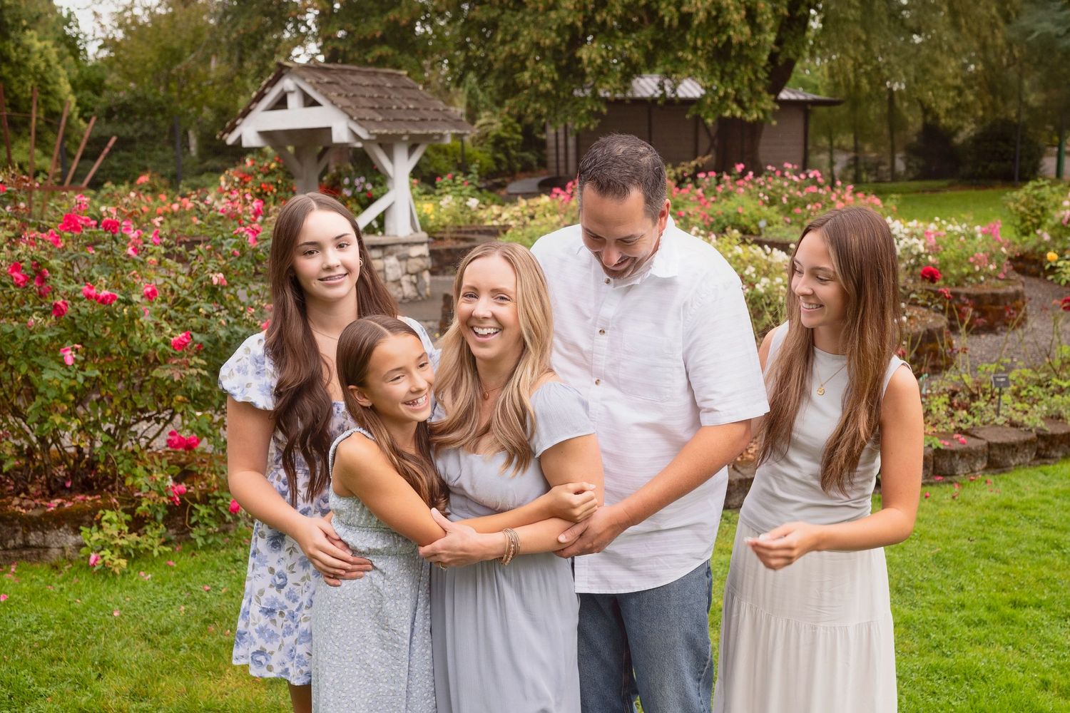 A group in coordinating blue and white outfits poses together on a lush green lawn for outdoor family photos.