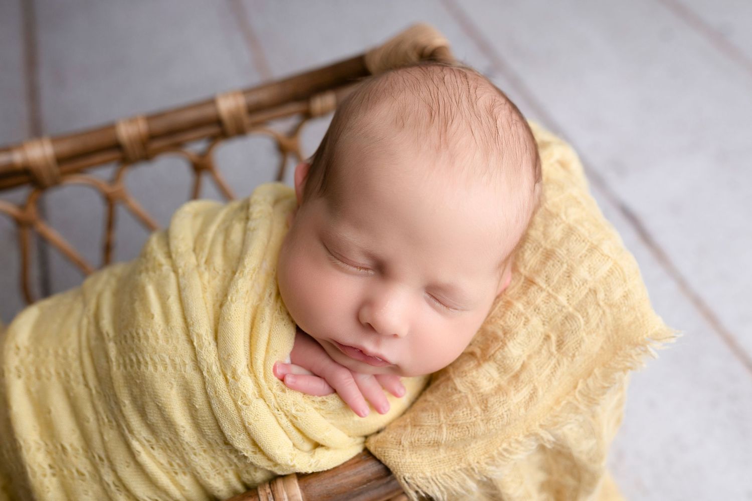 Newborn baby swaddled in yellow wrap sleeping peacefully in a small wooden basket.