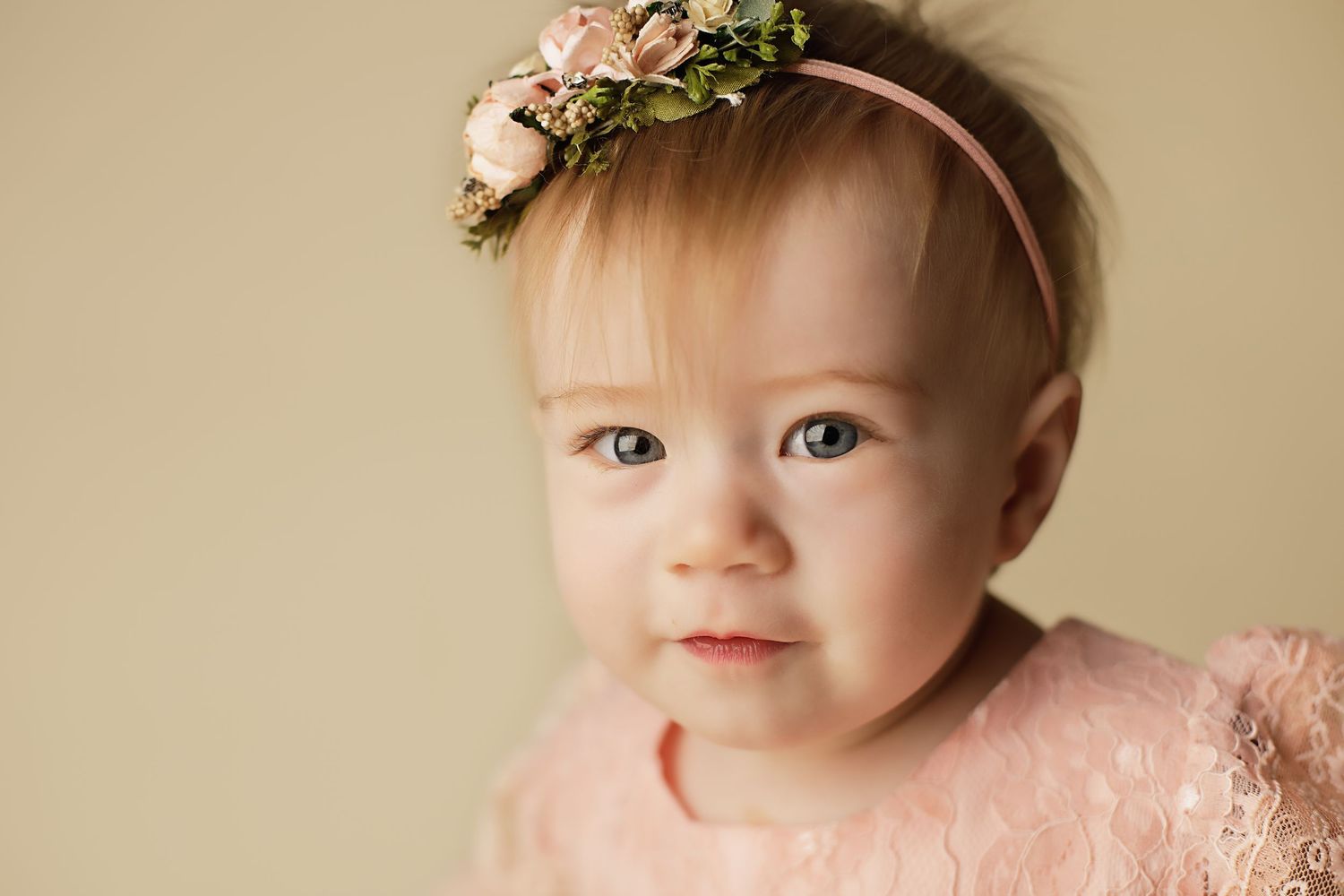 A sweet baby wearing a pink headband smiles while sitting for a series of adorable portrait photos.