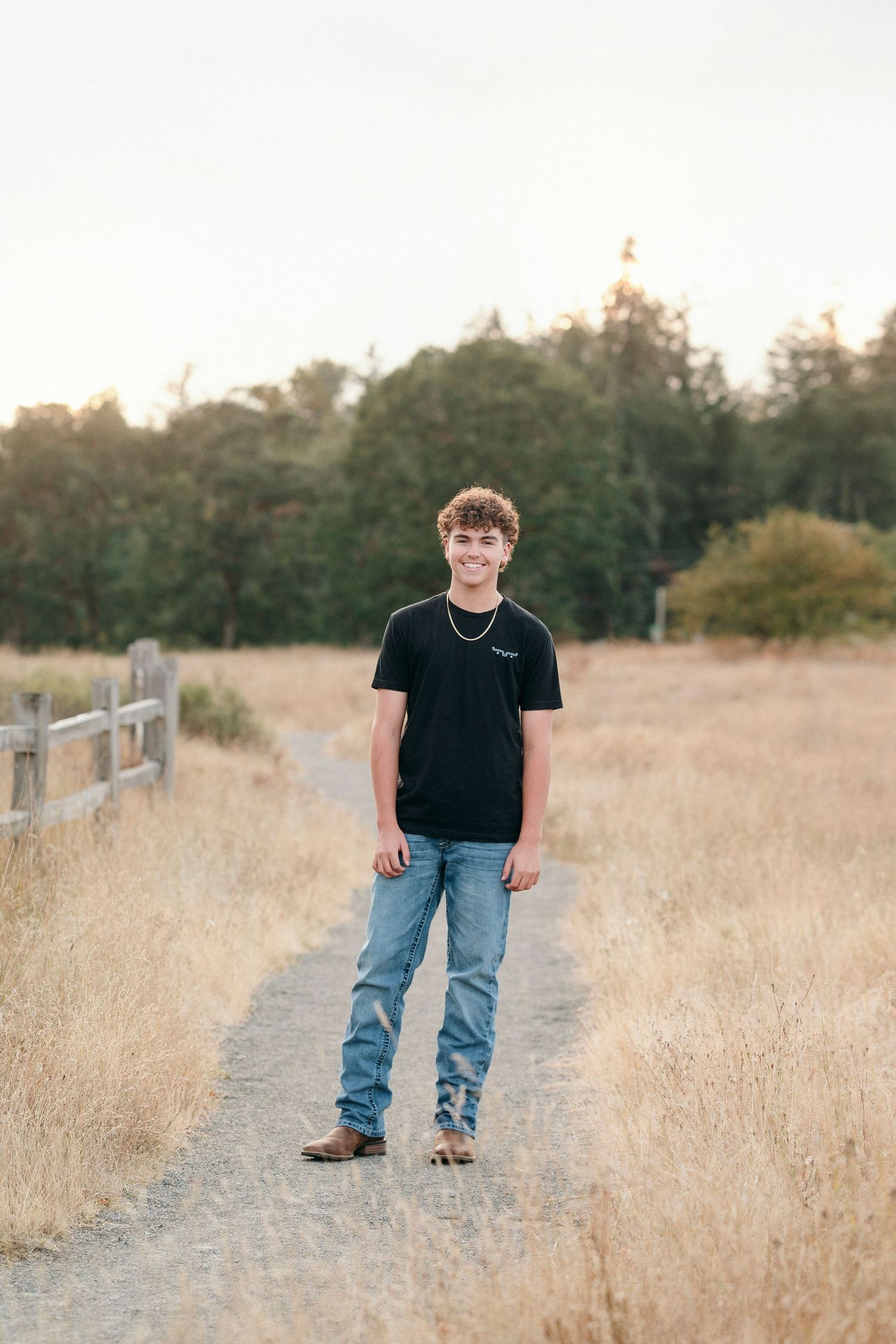 Outdoor photoshoot along a wooden fence path surrounded by tall golden grass.