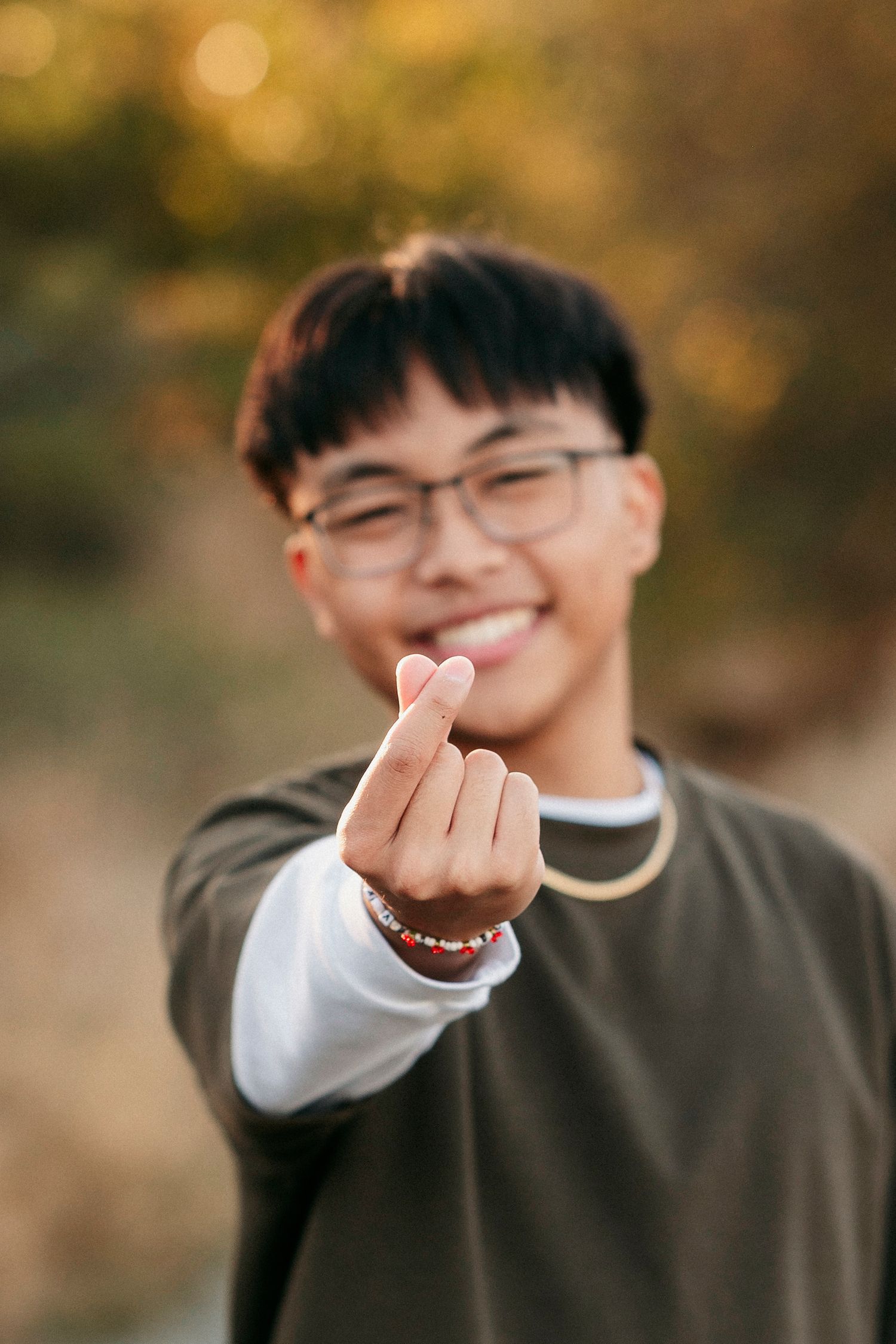 A sequence of photos showing someone making heart shapes with their hands against a warm autumn background.